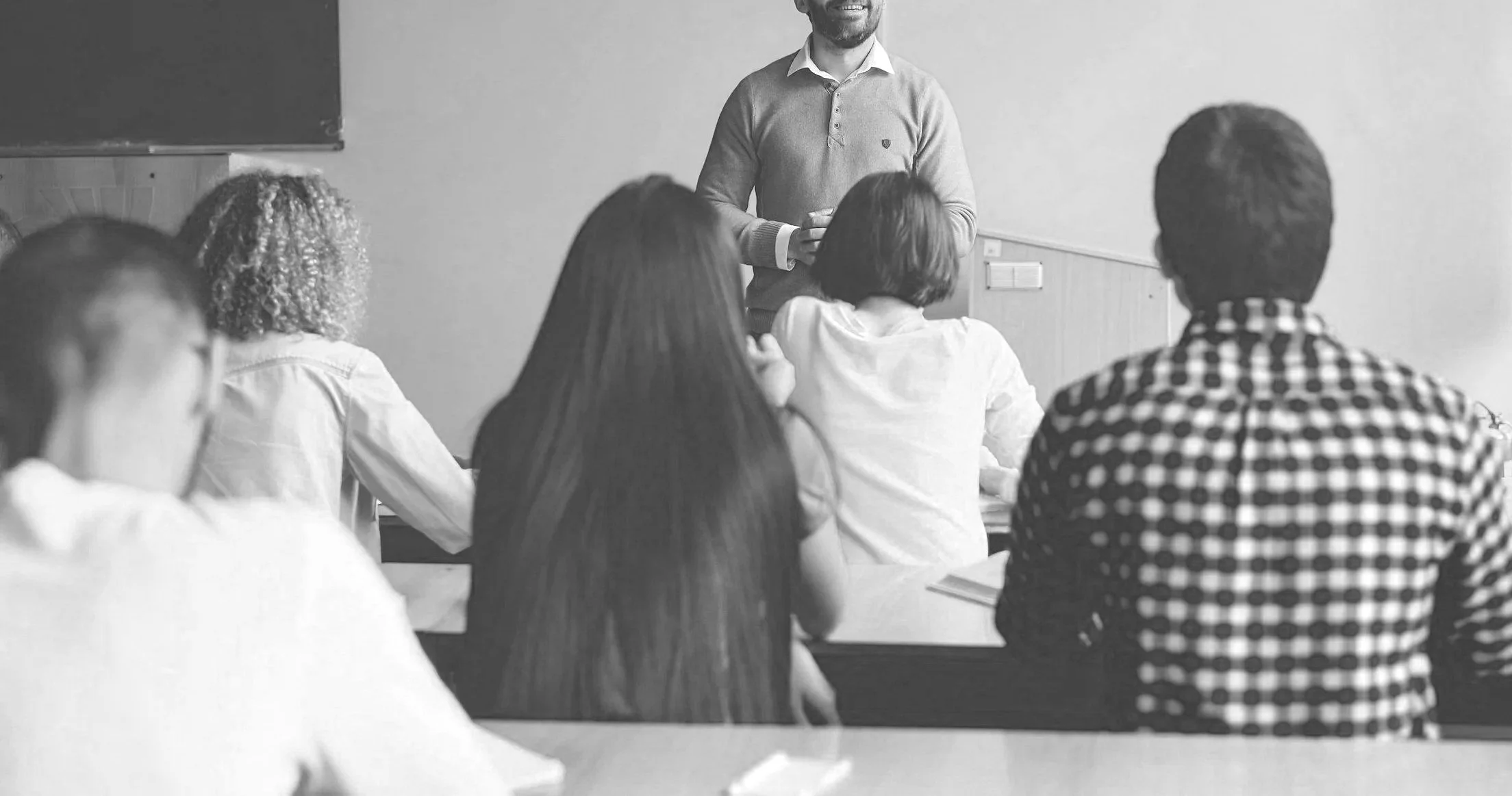 A man giving a presentation to a group of people in a classroom or meeting room, with the audience seated and listening attentively.