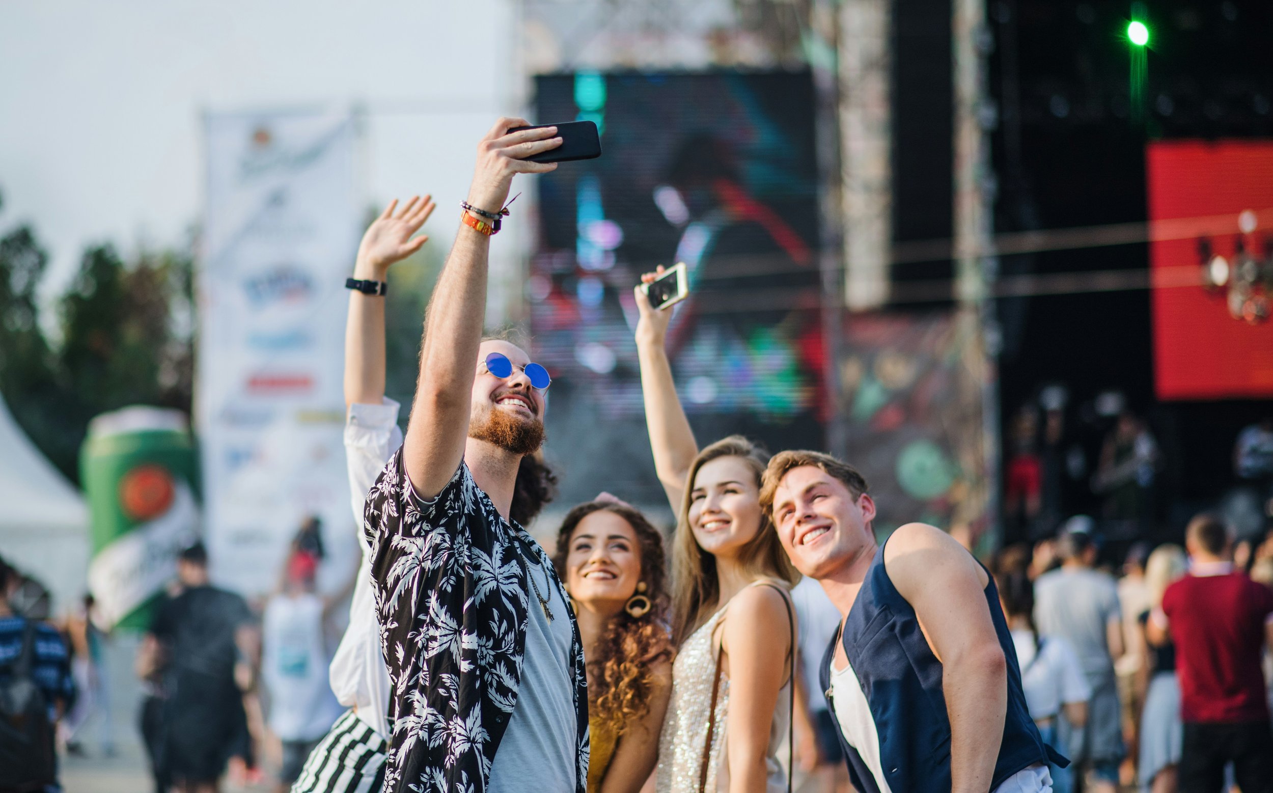 Group of young people taking a selfie on stage at an outdoor music festival.