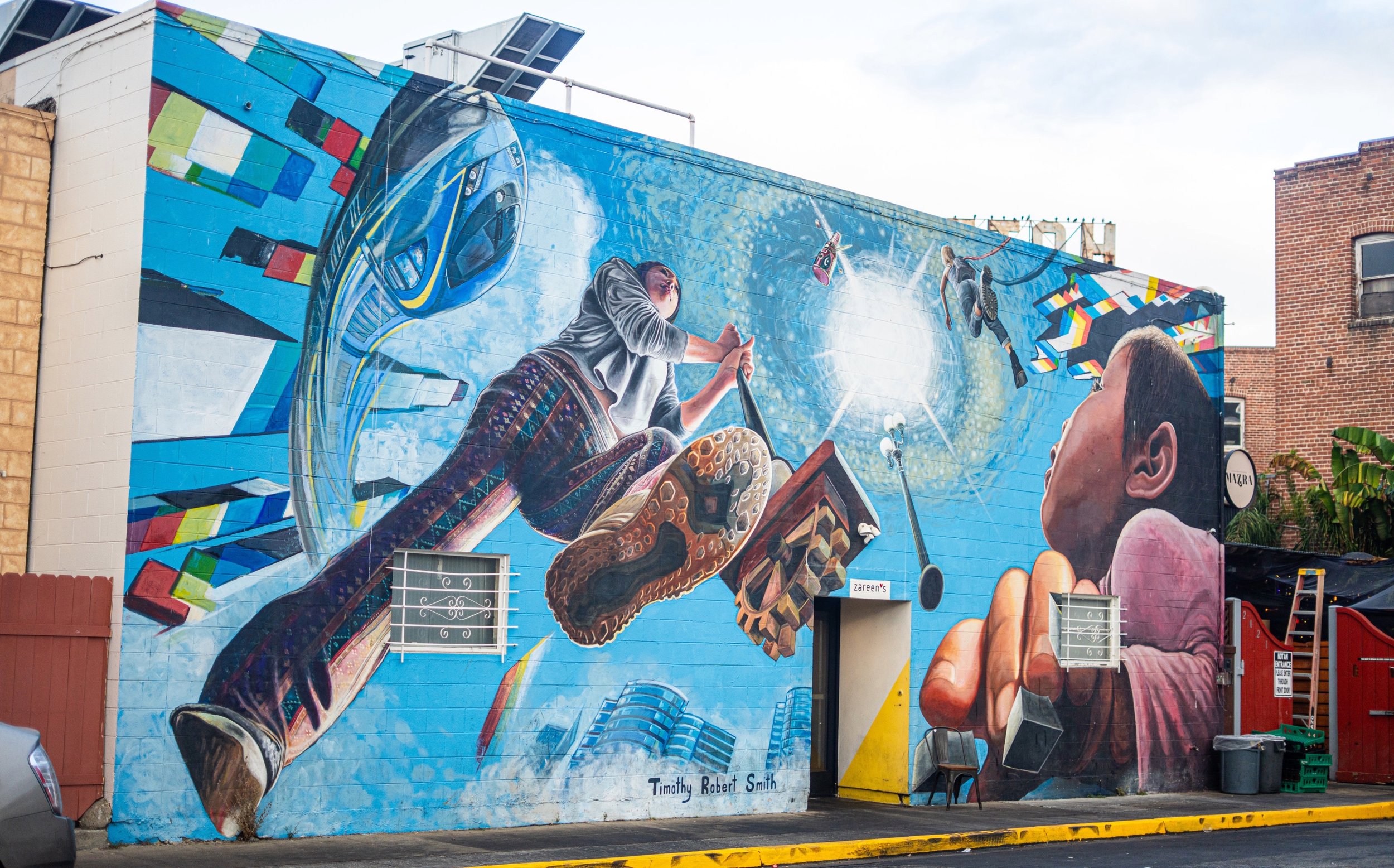 In 2023, Southern California artist Timothy Robert Smith painted ‘Mural Effect IV’ behind the the Pakistani-Indian restaurant Zareen. This mural is part of his series painting in different cities and incorporating perception as the core of his work.
