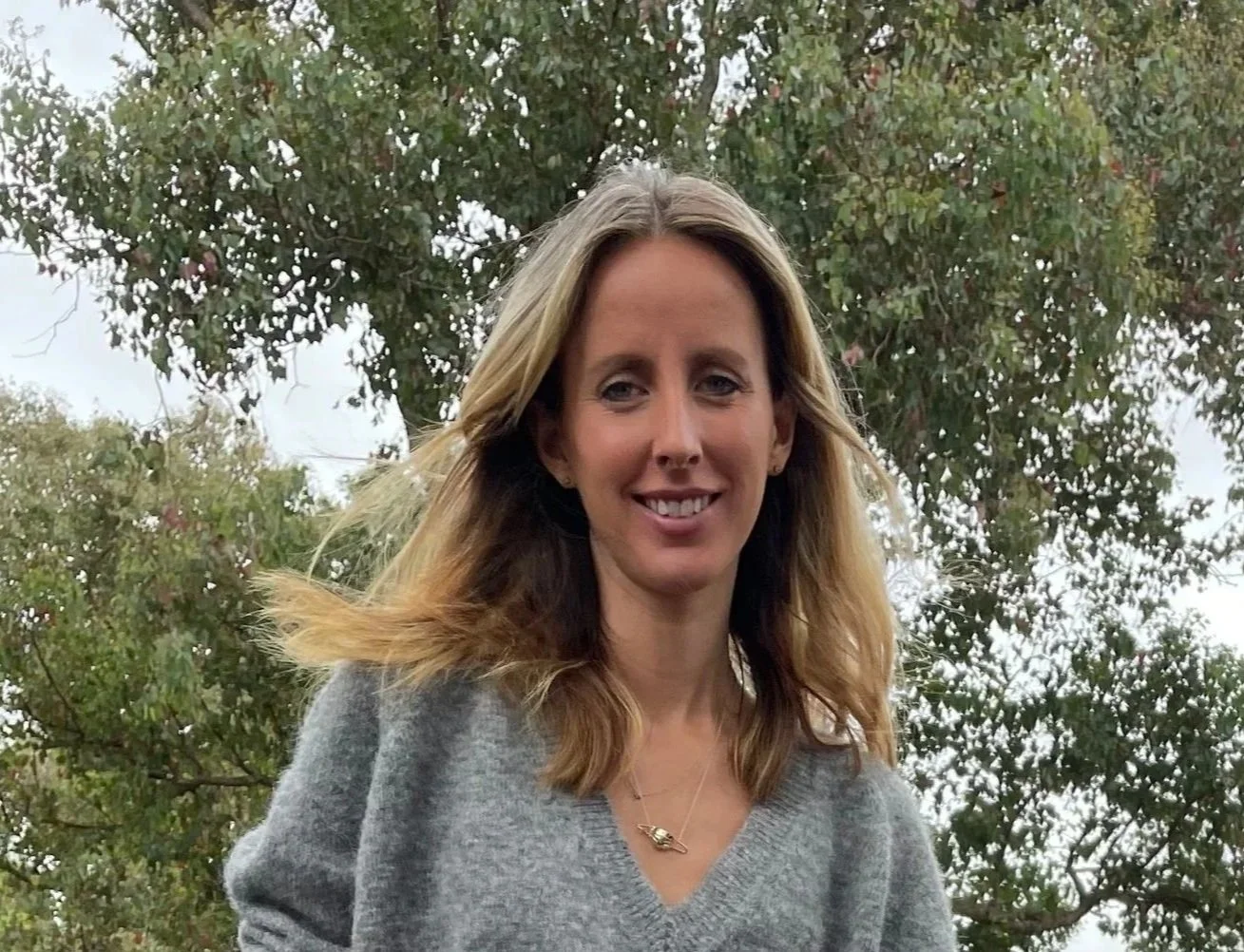 A woman with shoulder-length blonde hair smiling outdoors with trees in the background. Phoebe Bell