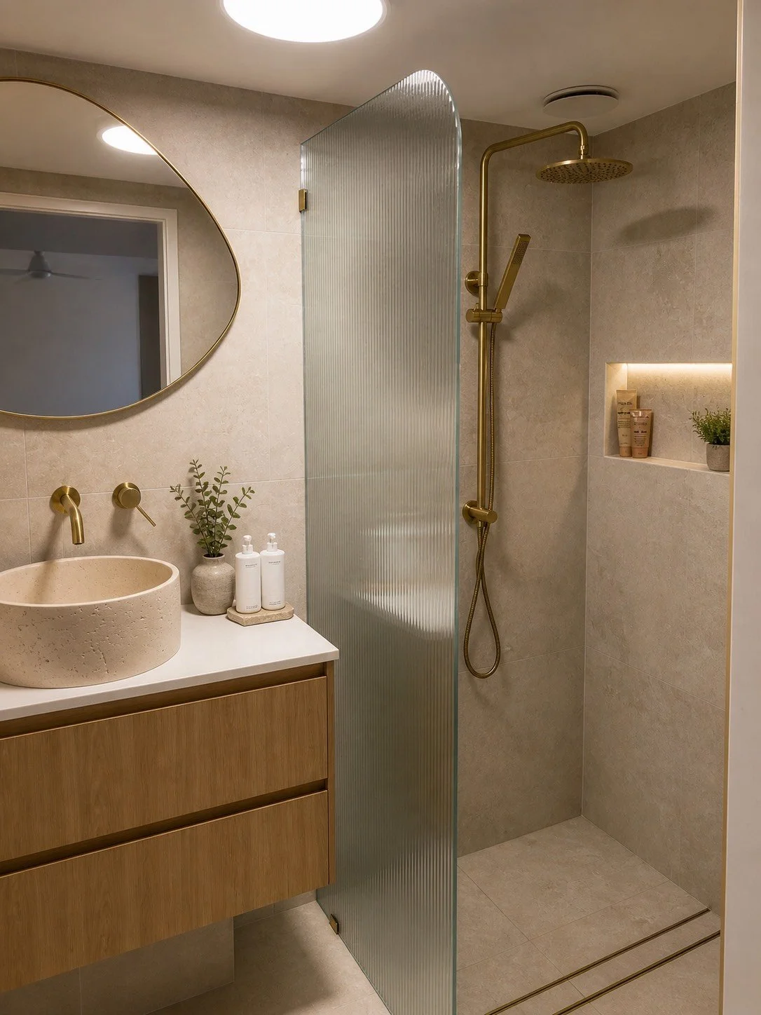 Modern bathroom with a round vessel sink, wooden vanity, gold fixtures, and a walk-in shower with a ribbed glass divider and a built-in shelf.