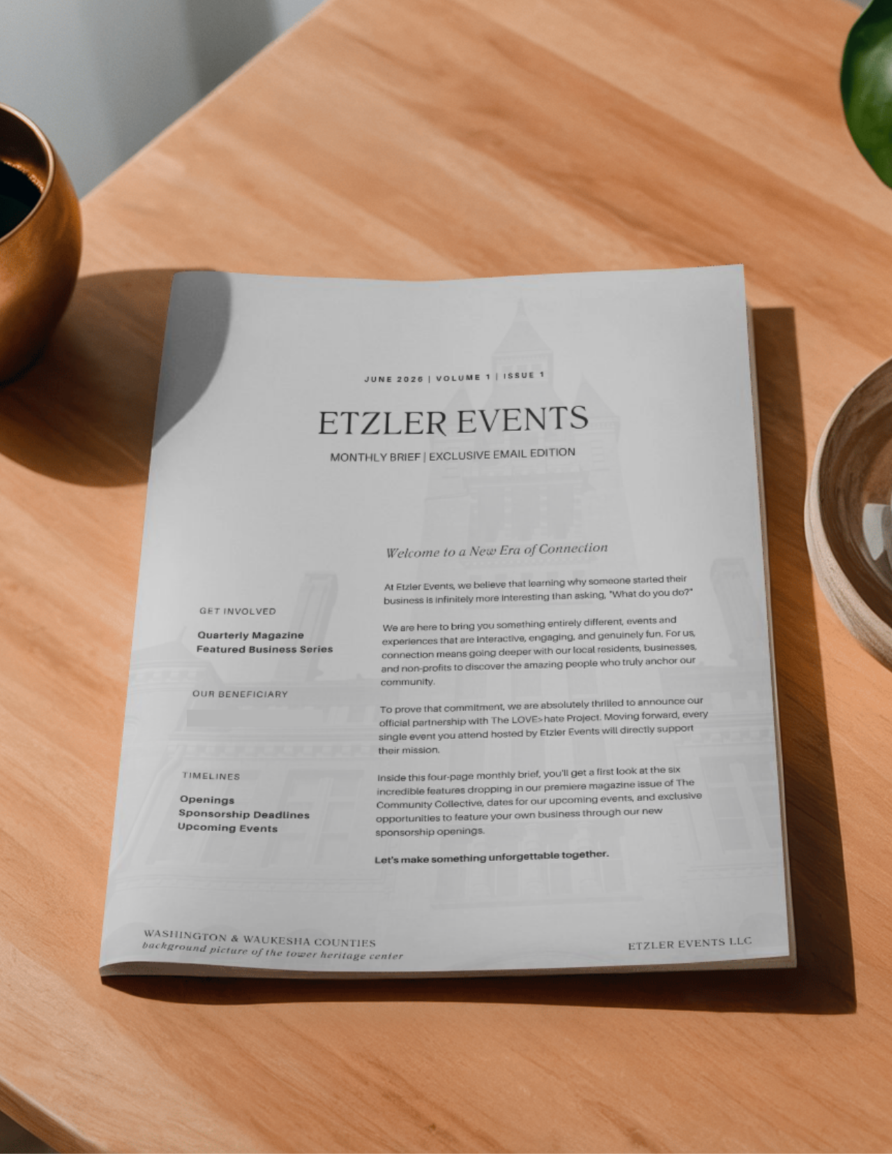 A printed newsletter titled 'ETZLER EVENTS' on a wooden table, with a cup of coffee or tea on the side and a green plant partially visible in the top right corner.