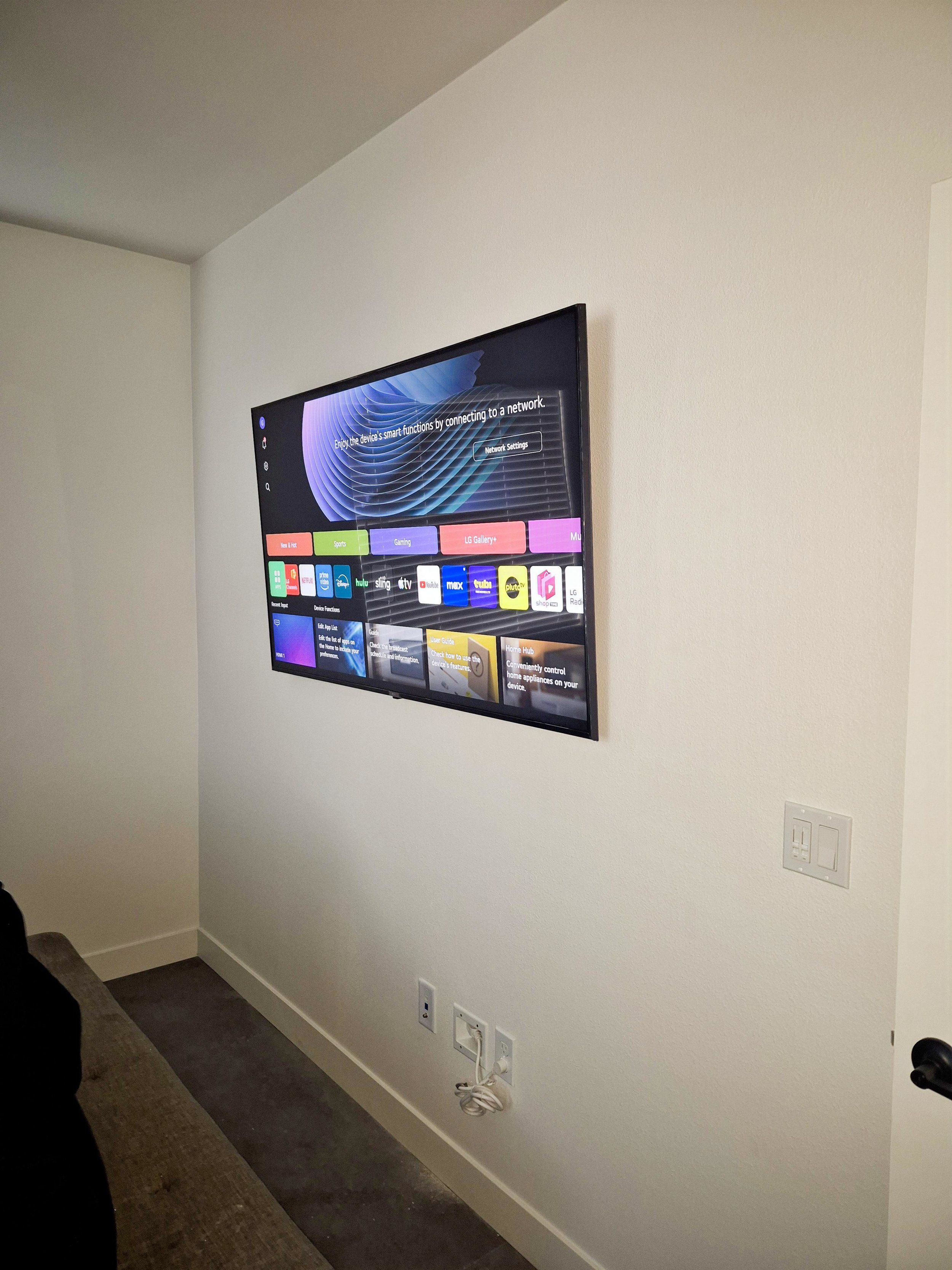 A flat-screen TV mounted on a white wall in a room, displaying a home screen with various app icons and options.