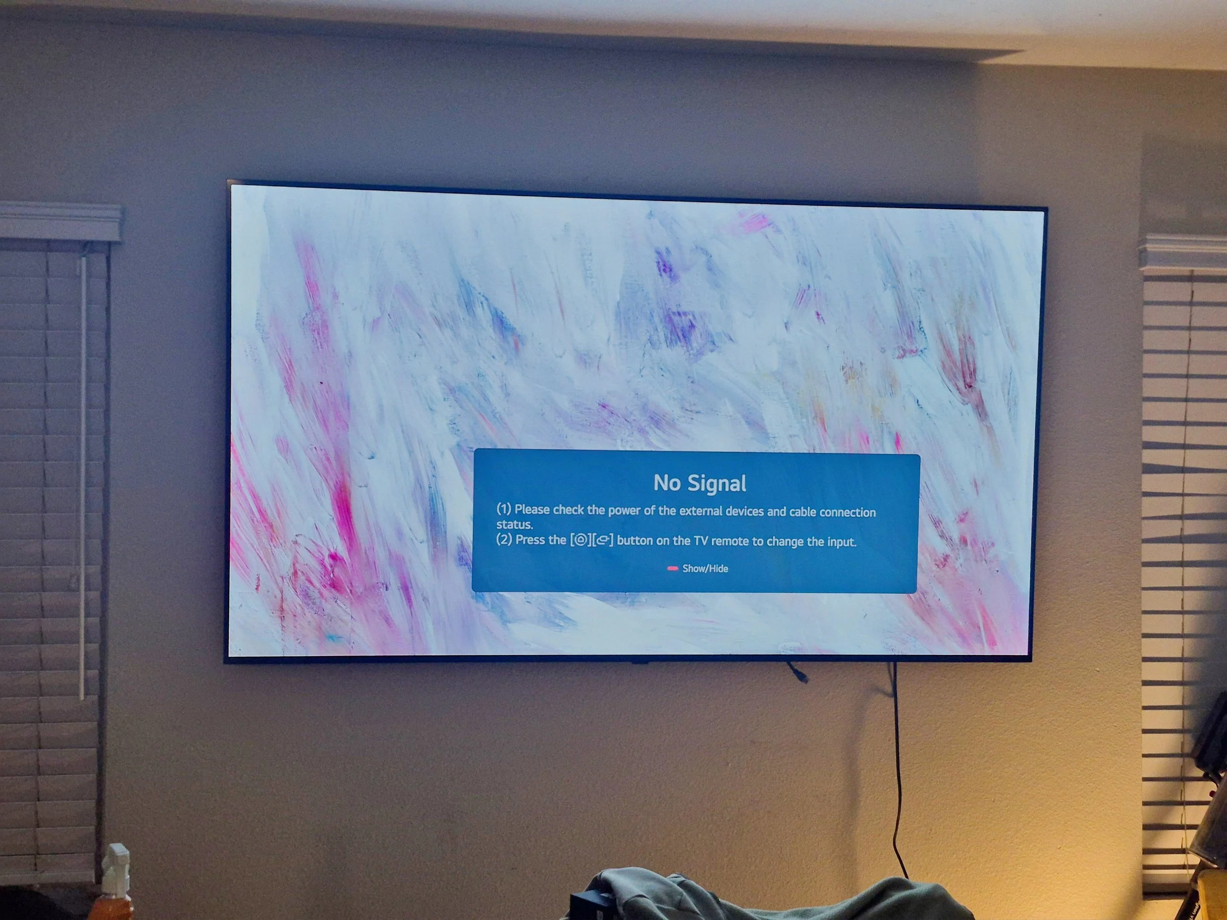 A television screen displaying a "No Signal" message with tips to check external device power and cable connection, set against a background of pink, blue, and white abstract artwork.
