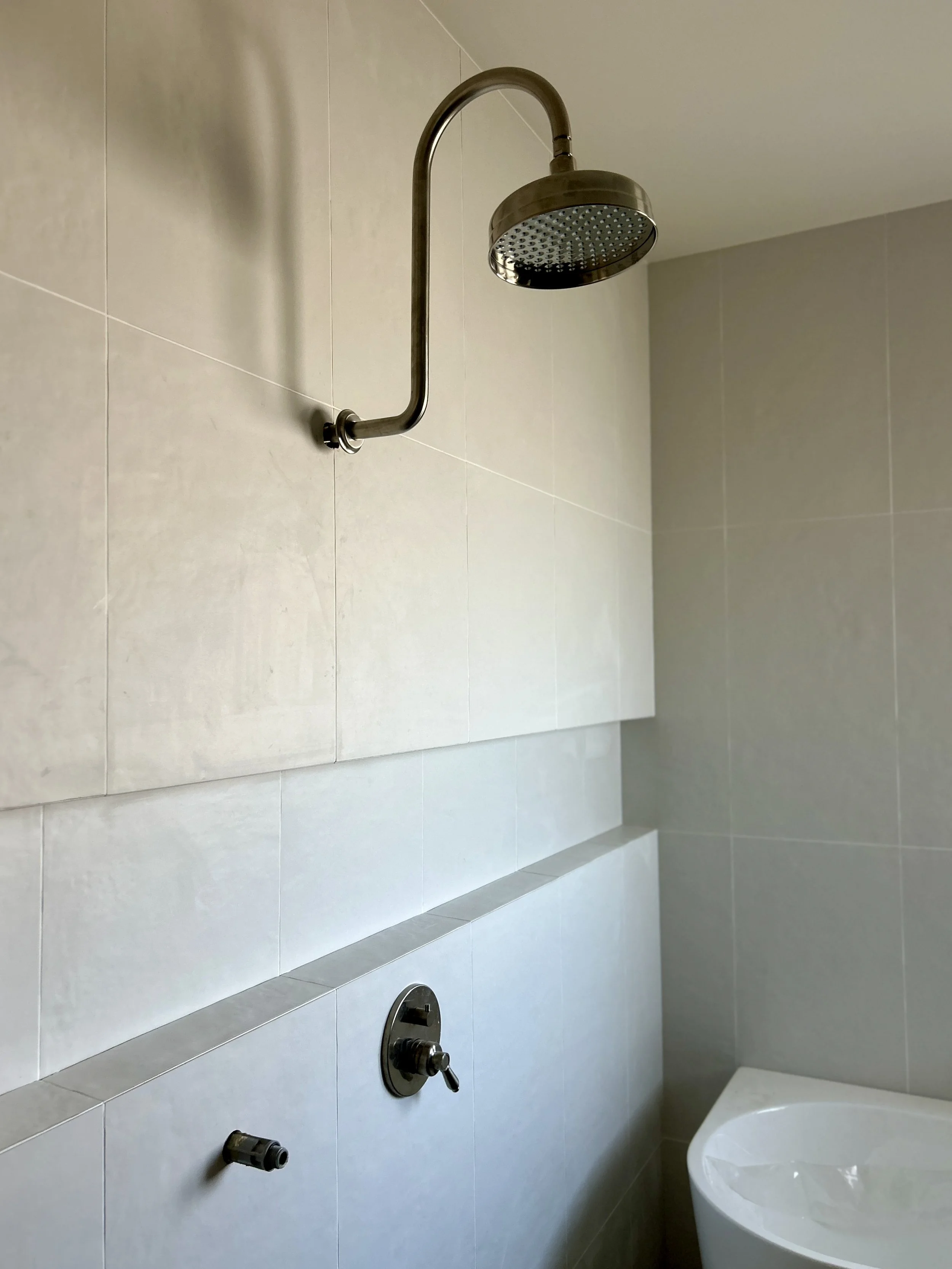 Bathroom shower with beige tiles, a large round showerhead, and a separate handheld shower fixture, no visible water.