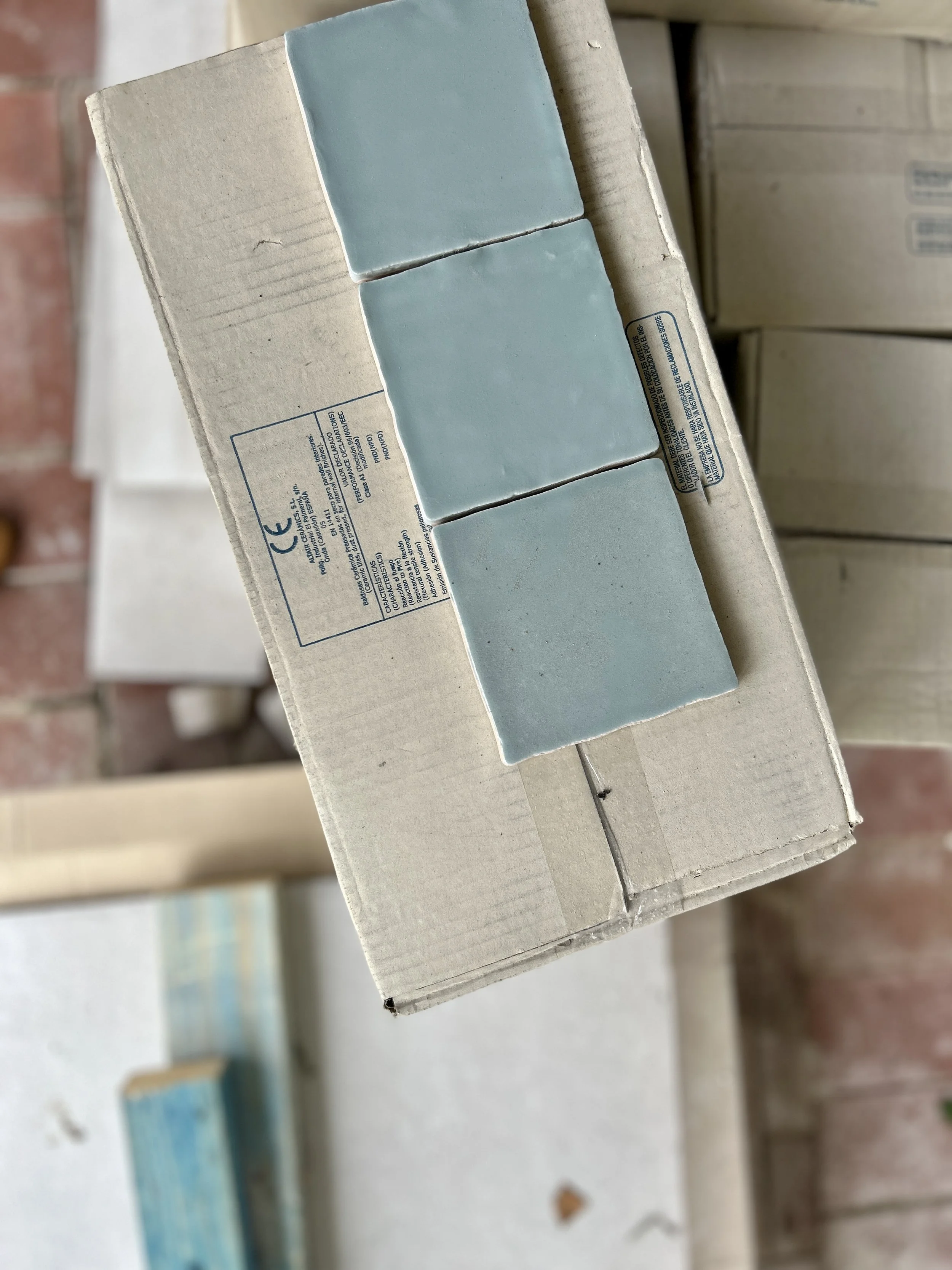 Stacked boxes with blue tiles on top, placed on a wooden surface.