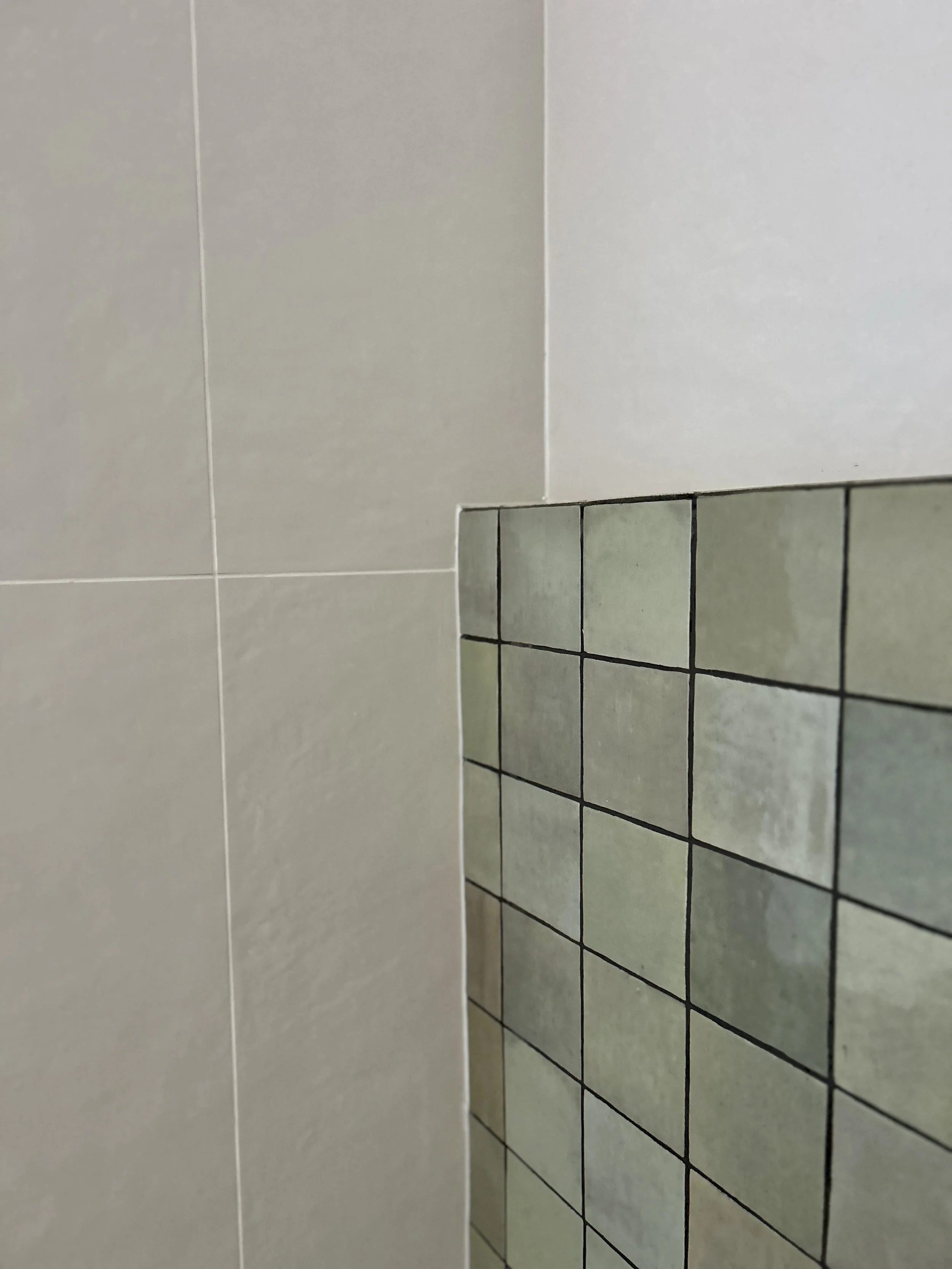 Close-up of tiled wall in a bathroom or kitchen, with a partial reflection of the tiles visible.