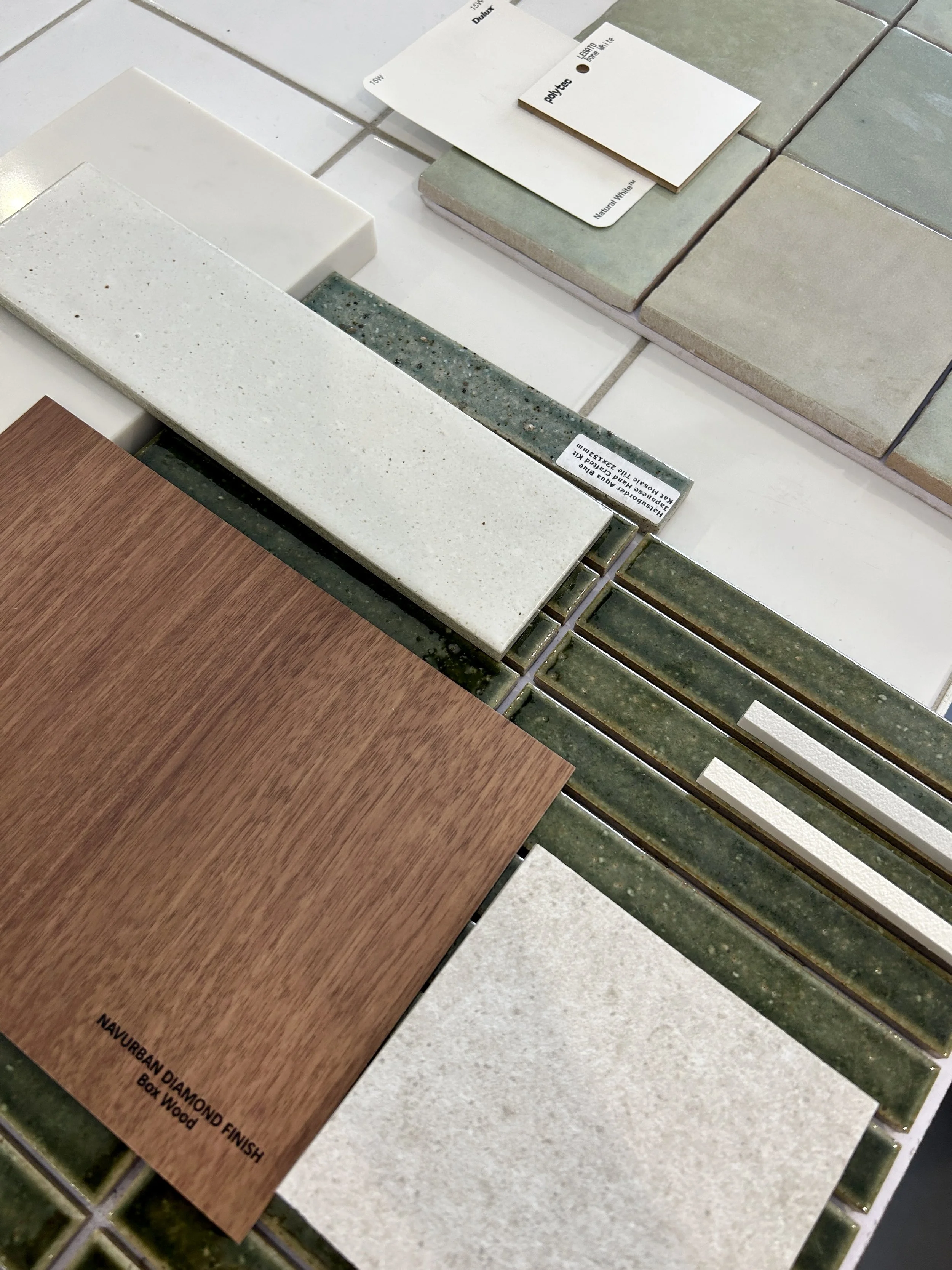 Various samples of tiles and laminate flooring, including ceramic tiles in beige, gray, and green shades, and a wood-look laminate board.