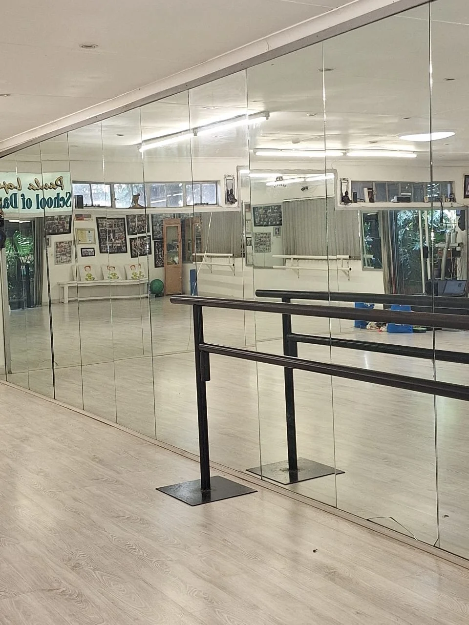 Empty dance studio with mirrored wall, ballet barre, and fitness equipment visible through the reflection.