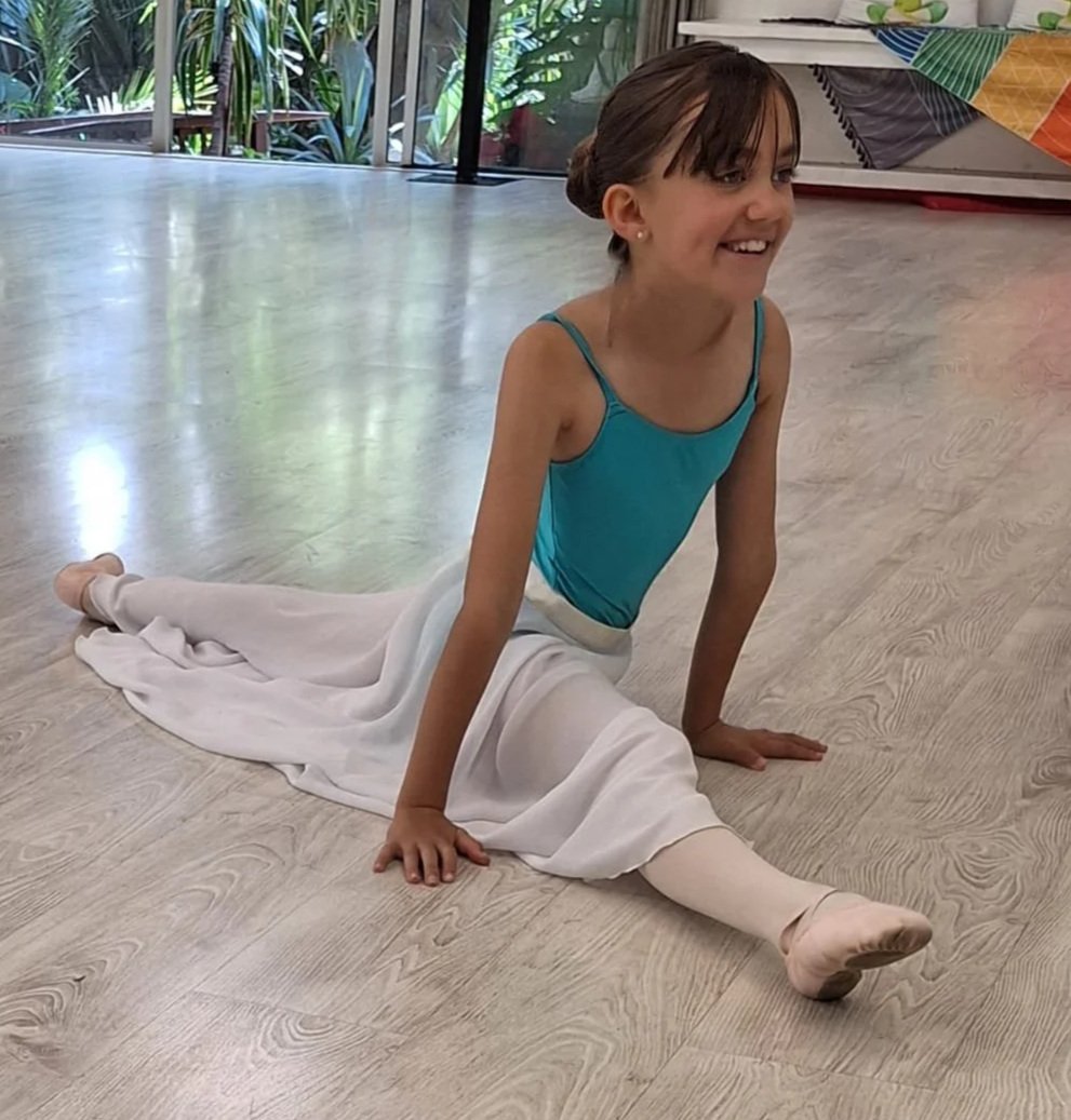 Young girl in a ballet costume performing a split on the floor of a dance studio.