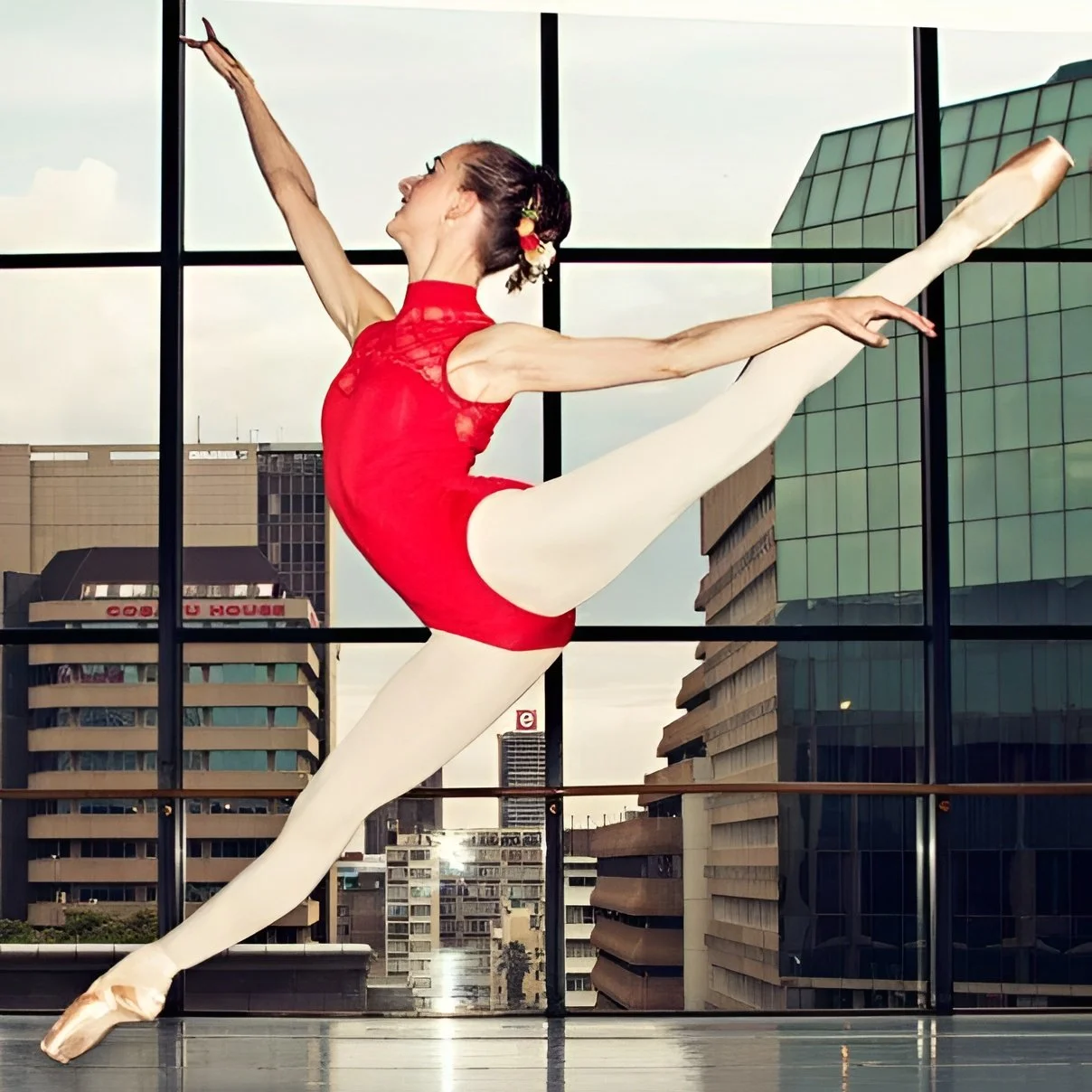 A ballet dancer performing a pose on stage with a purple background, wearing a black and gold tutu, pink tights, and pointe shoes.