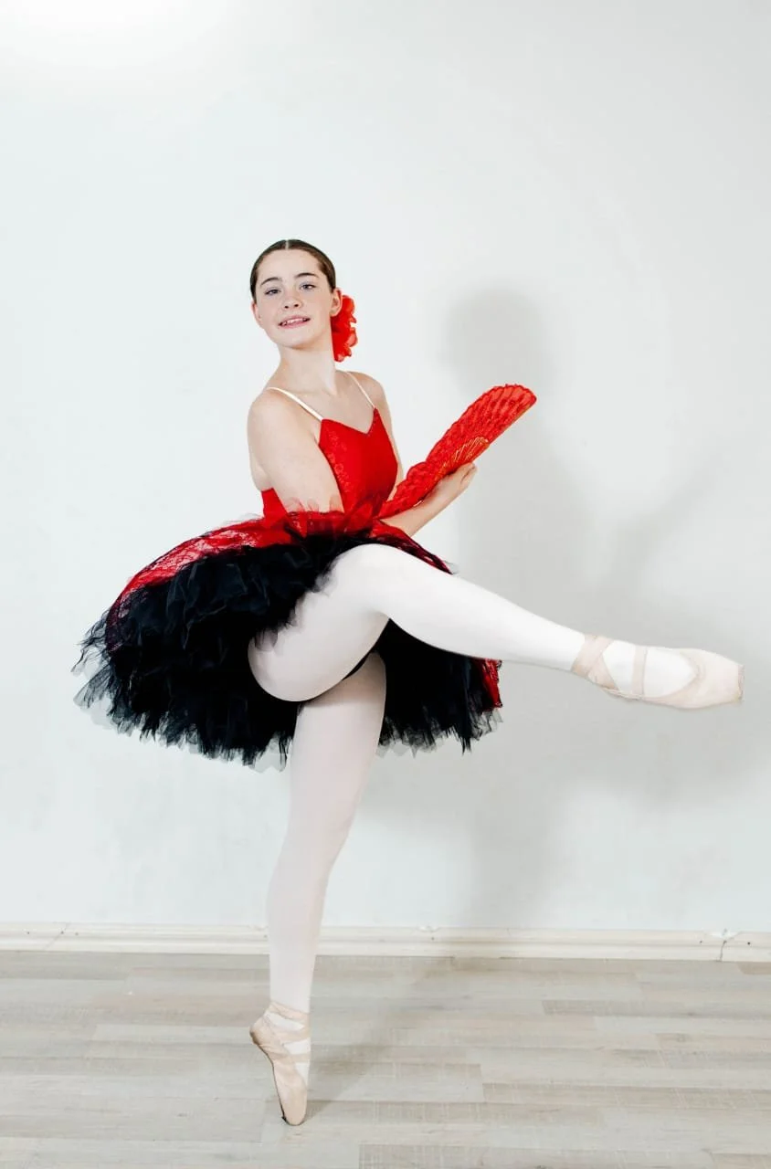 A ballet dancer in a red and black tutu with white tights and ballet slippers practicing ballet in a studio.