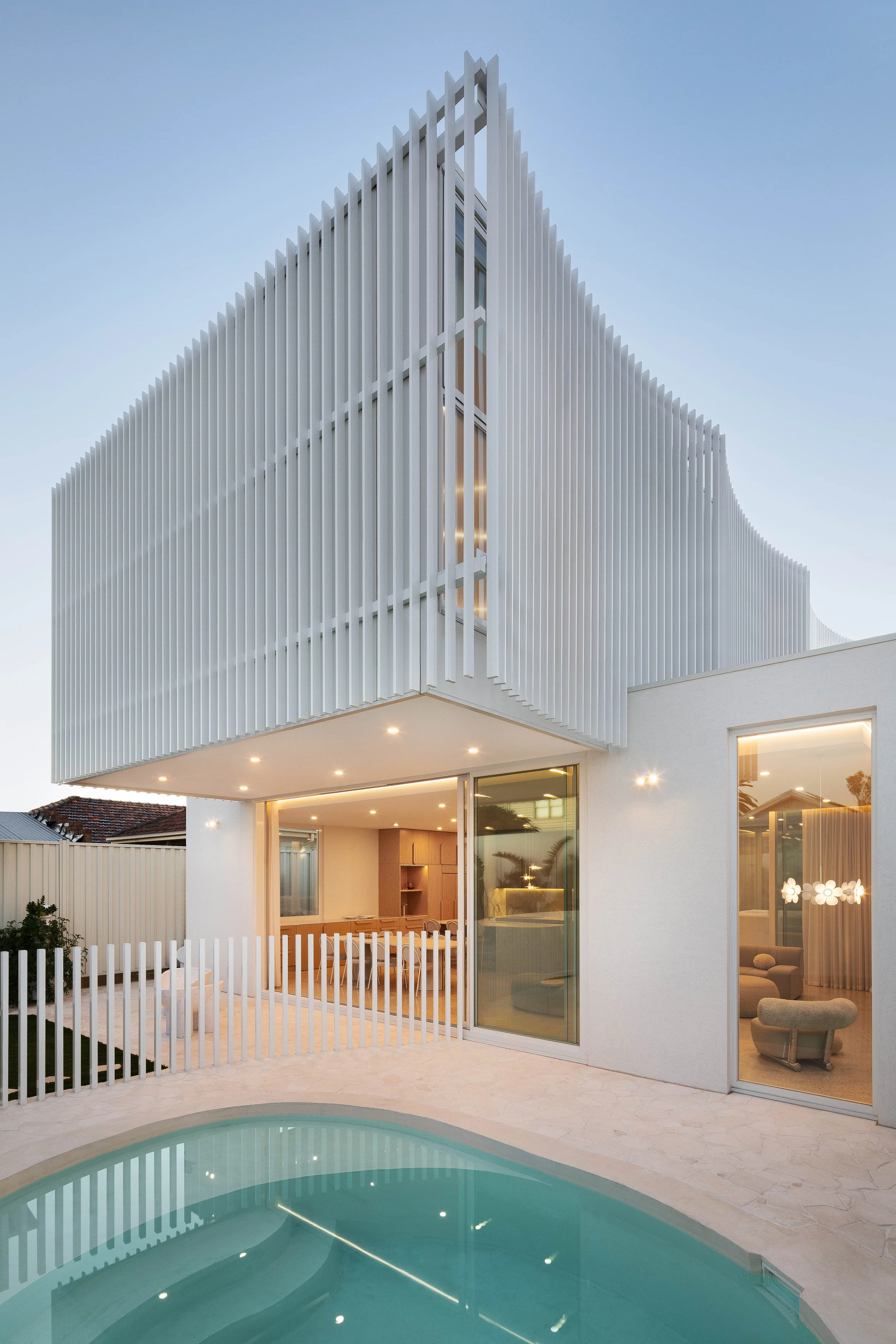 Modern white house with unique vertical slat exterior design, large glass sliding doors, and a swimming pool in the backyard.