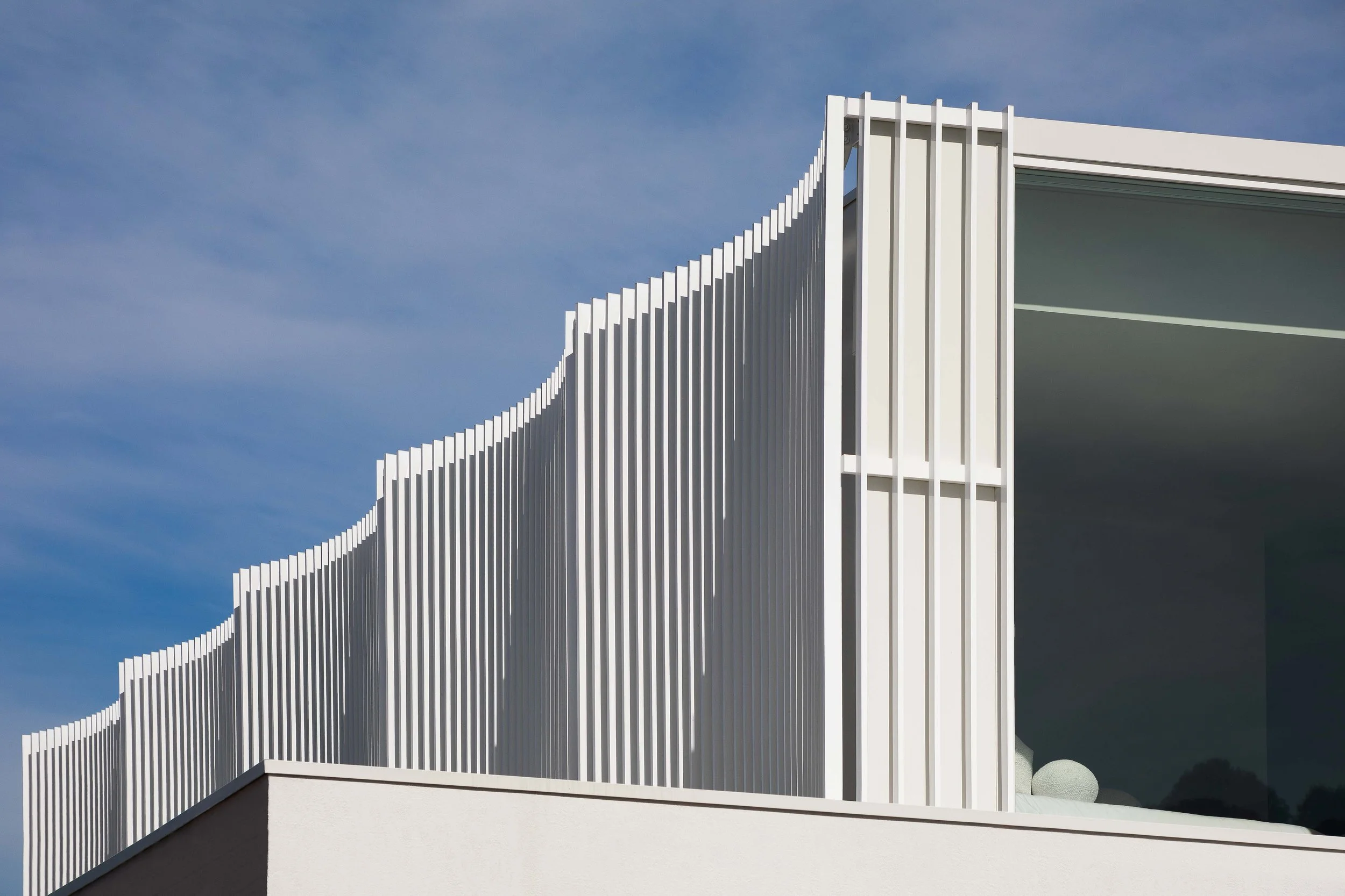 Modern building with white vertical louvered exterior and large glass window against a blue sky.