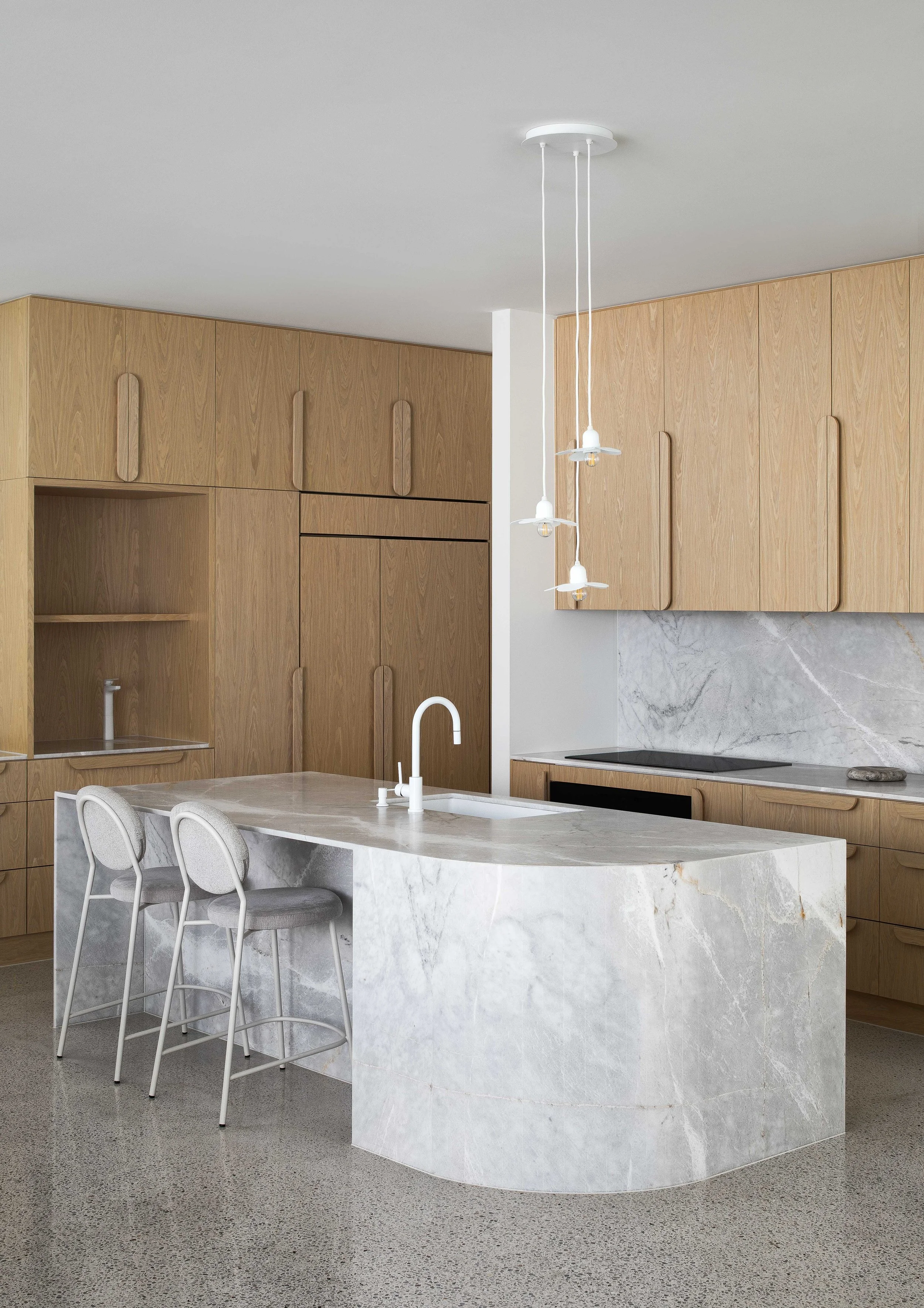 Modern kitchen with a marble island, light wood cabinets, a white ceiling, and three pendant lights over the island.