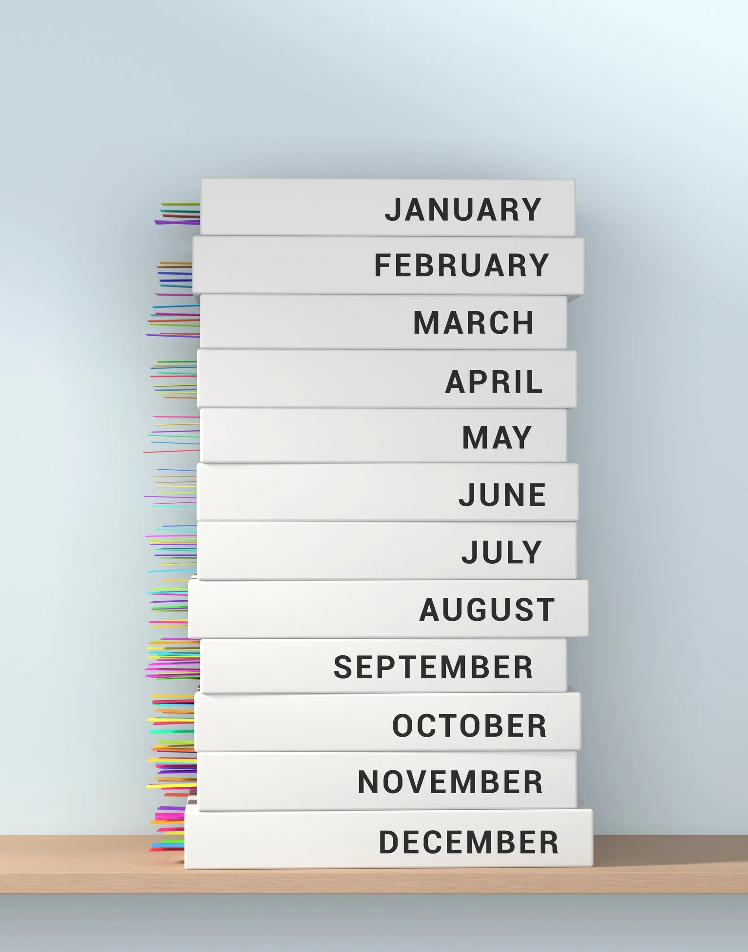 A wooden desk with an organized stack of twelve white boxes labeled with the months from January to December. The boxes have multicolored paper clips protruding from their sides, each matching the month's label.