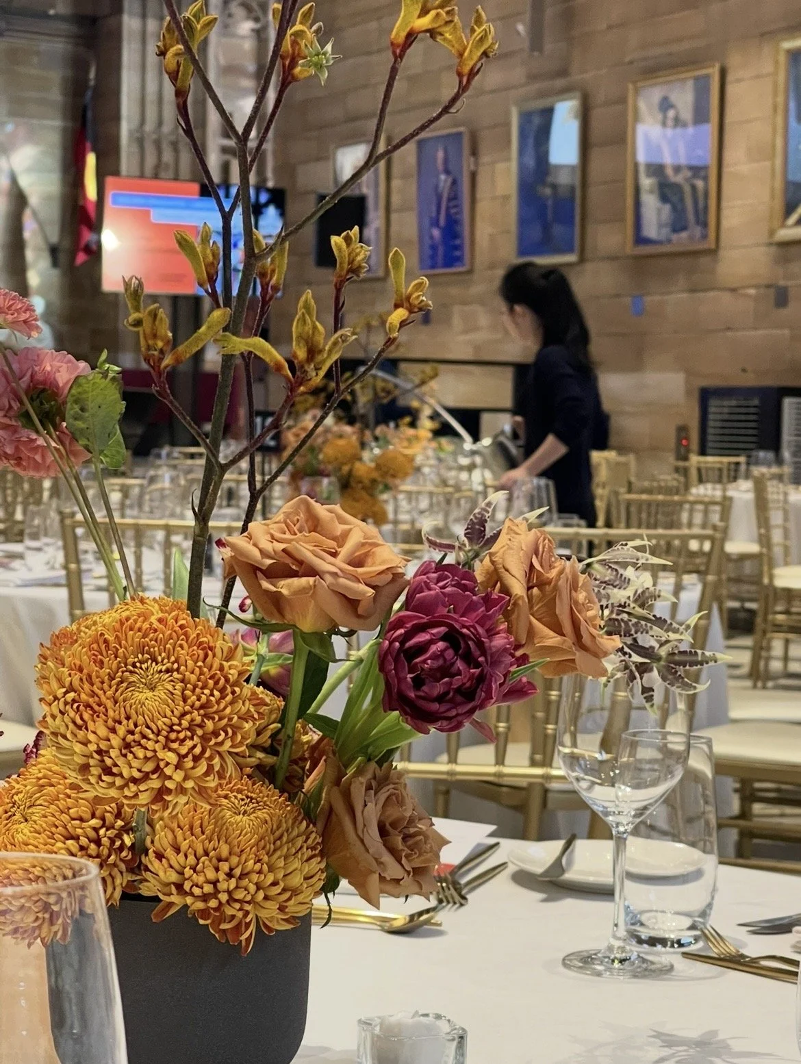 A floral centerpiece with orange, purple, and pink flowers on a banquet table set for an event in Sydney