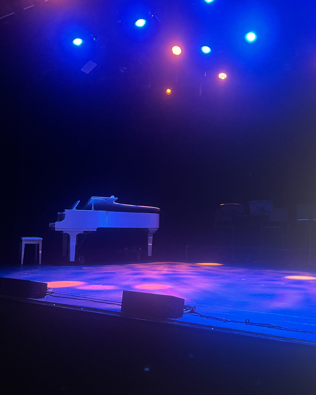 White, elegant grand piano, surrounded by blue and purple stage lights, behind the scenes before a Pursuit 19 event