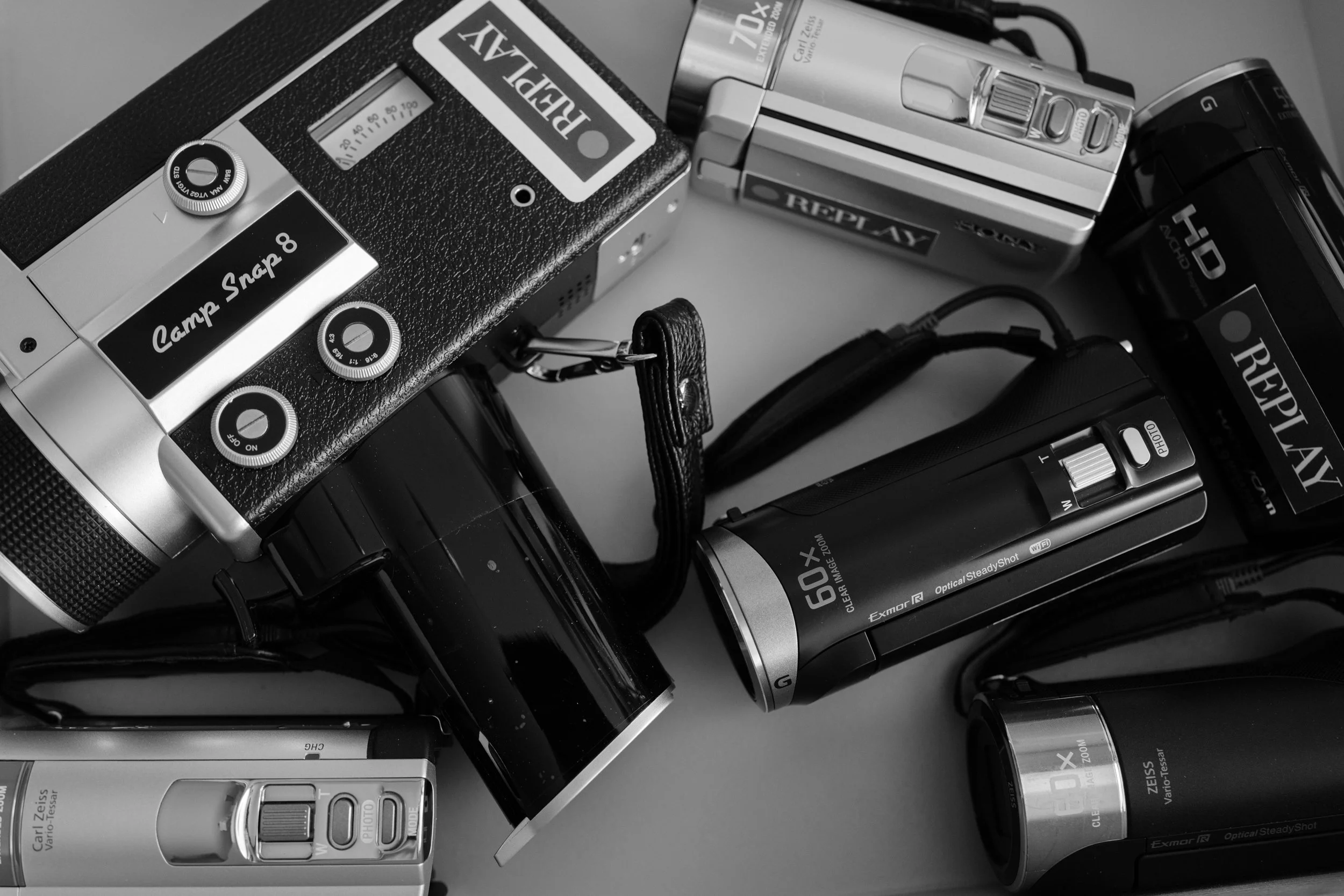 Retro camcorder rentals here camera bar box .Multiple vintage cameras and camera accessories scattered on a surface, mostly in black and white.