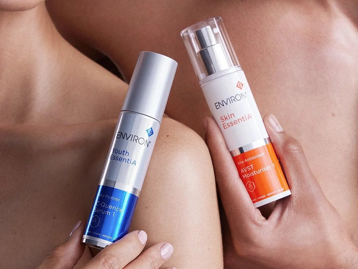 Two skincare serum bottles held by hands over bare skin and shoulder.