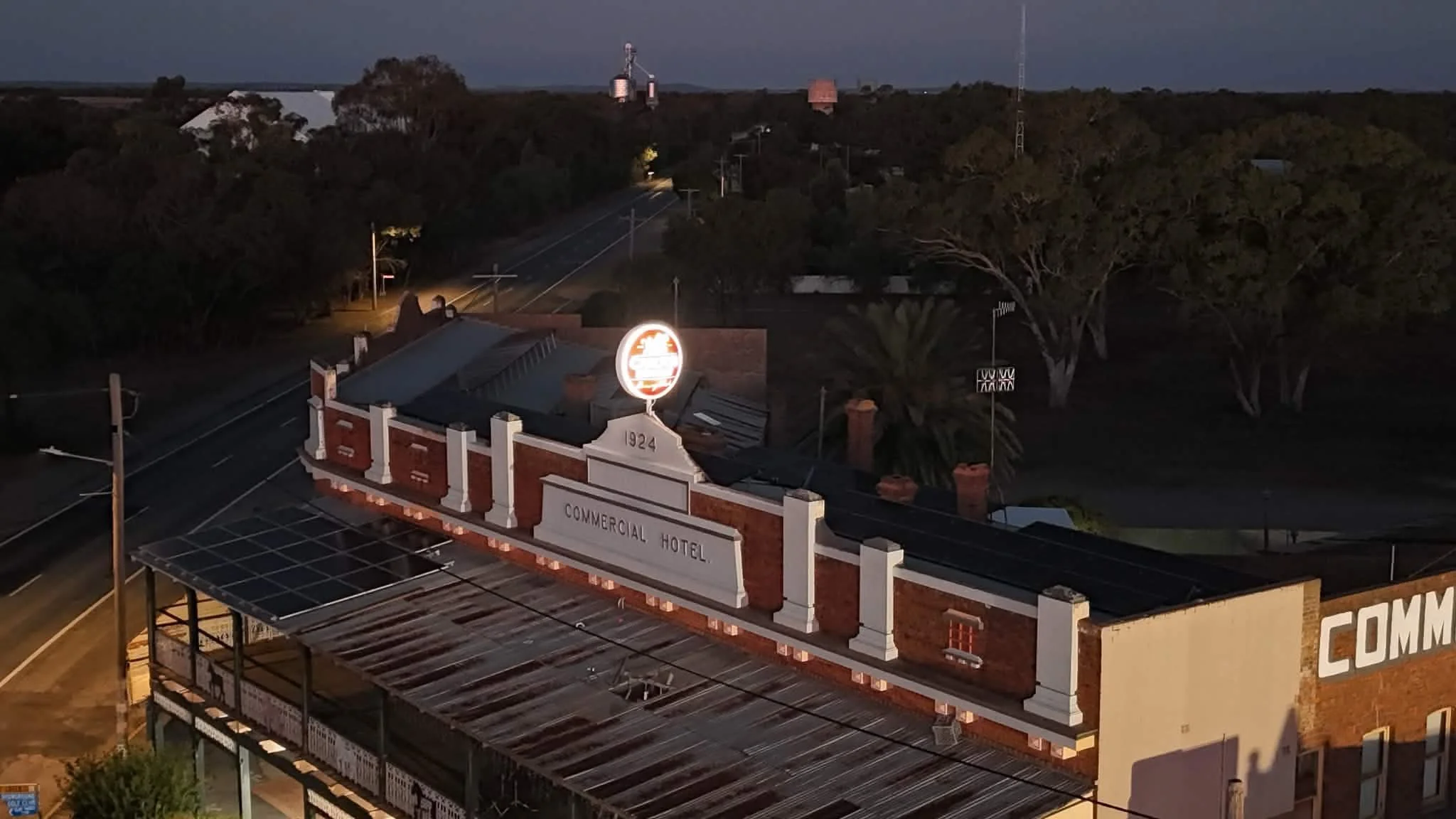Night view of a commercial hotel building with vintage signage, trees, and a dark sky in the background.