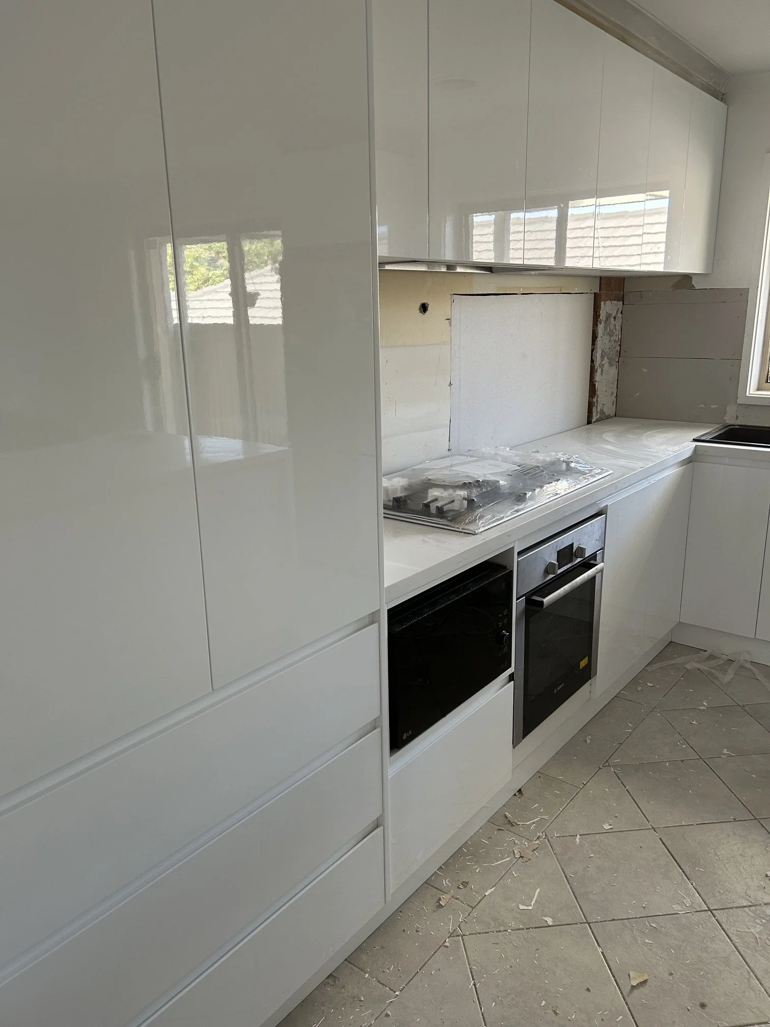 Kitchen under renovation with white cabinets, a gas stove, and construction debris on the tiled floor.