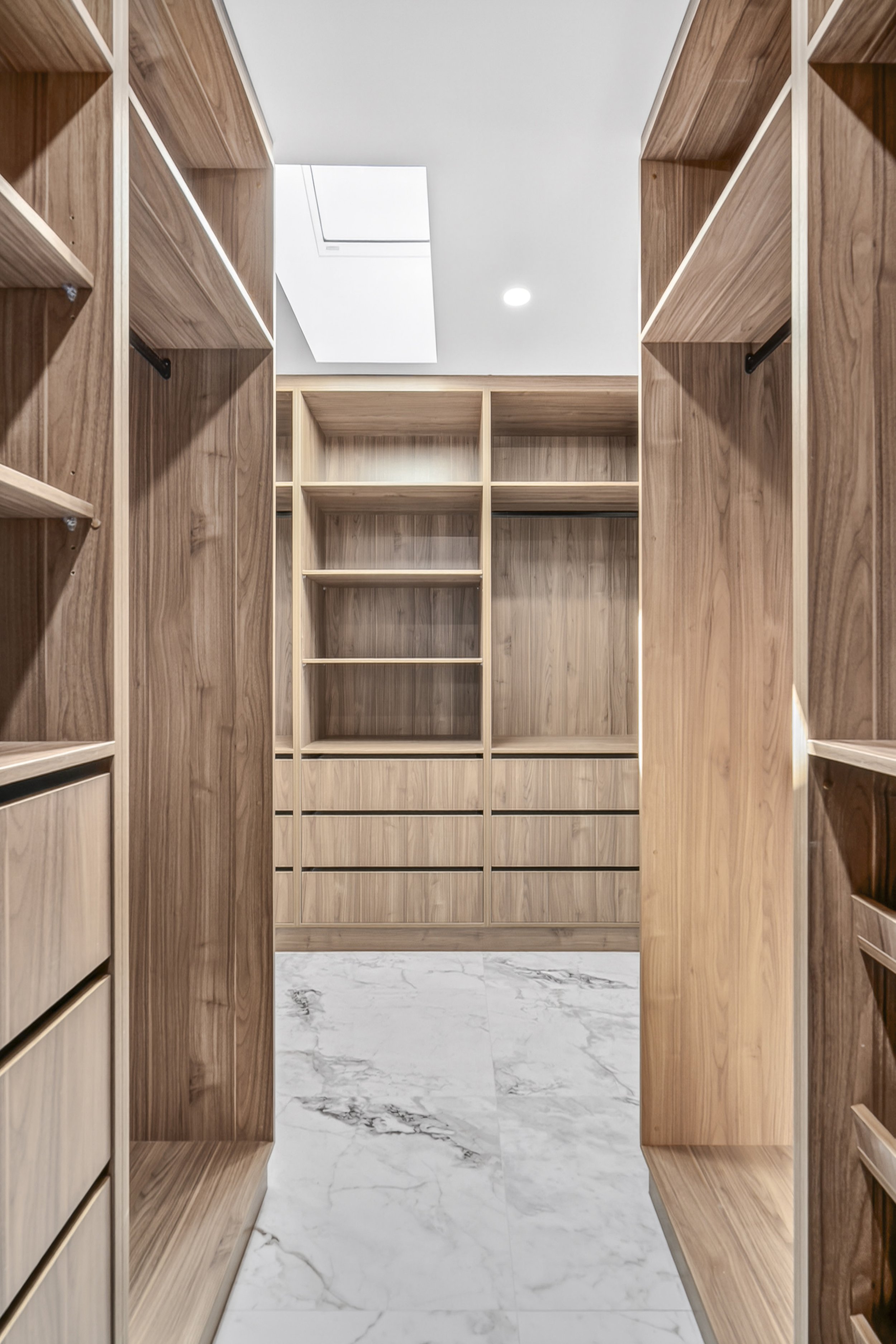 Empty walk-in closet with bare wooden shelves and drawers, marble floor, and ceiling light.