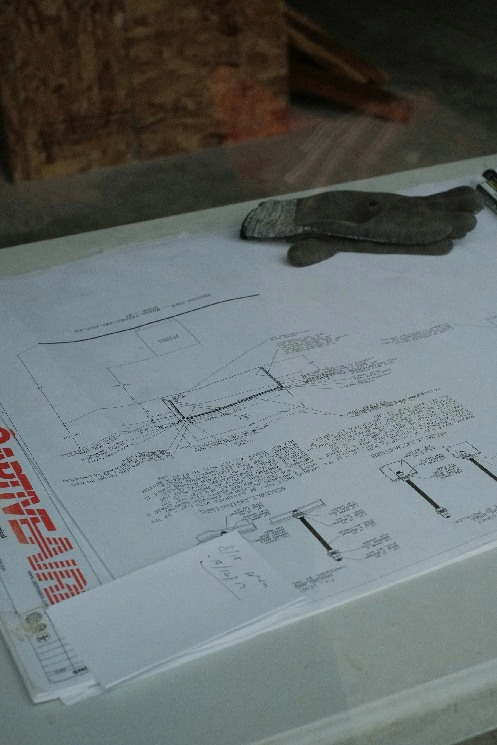 Blueprint or architectural plan on paper, with a work glove and a marker on top, resting on a table or surface.