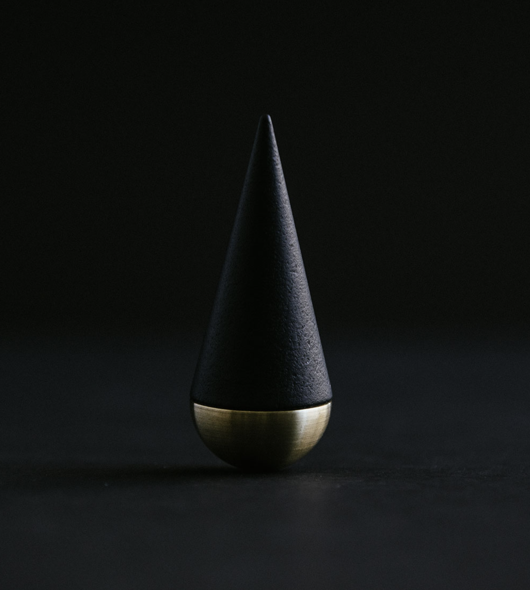 A close-up view of a metallic pin with a pointed tip, mounted on a round metallic base, against a black background.