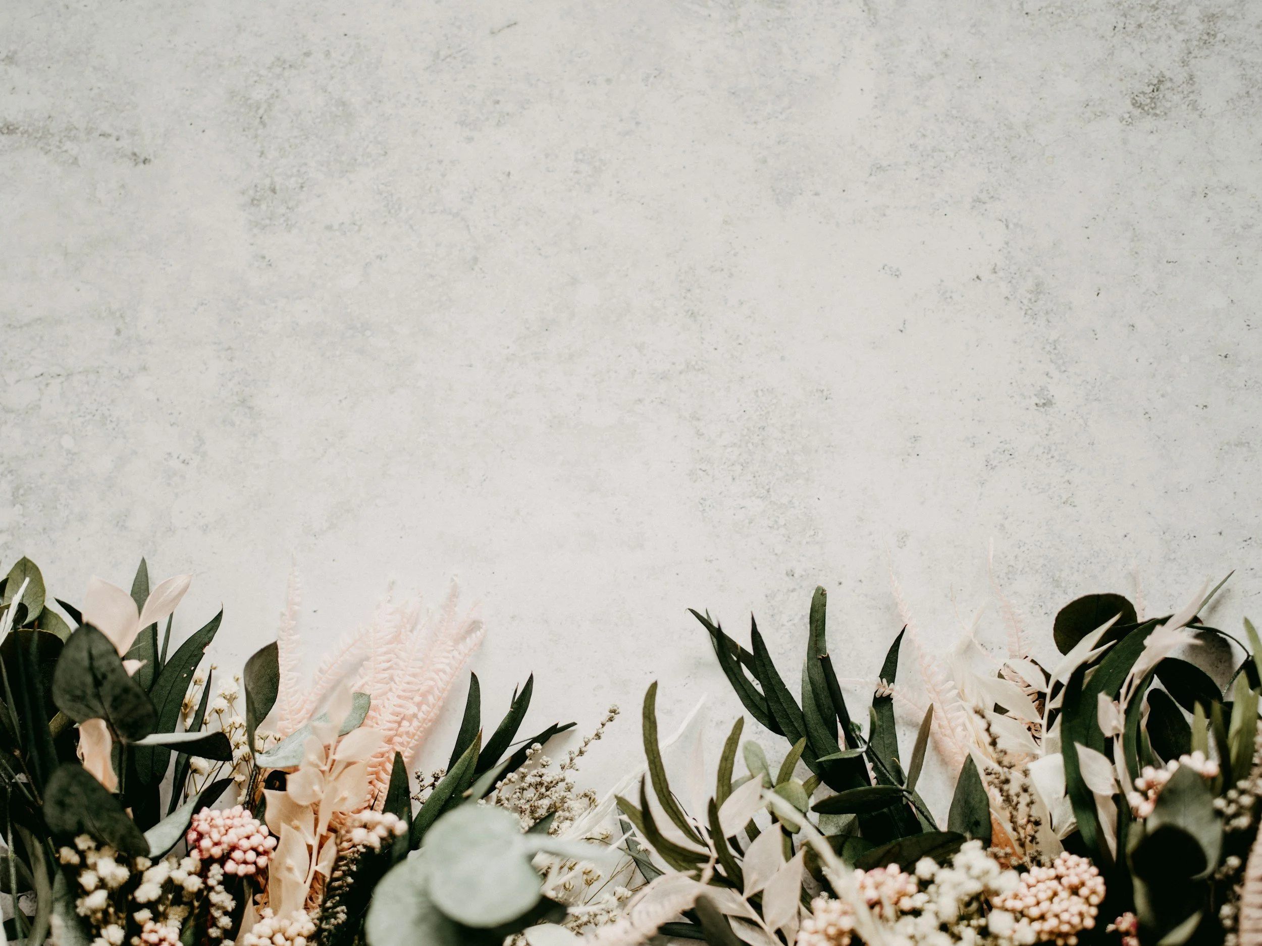 Decorative floral arrangement of various flowers and greenery at the base of a textured wall.
