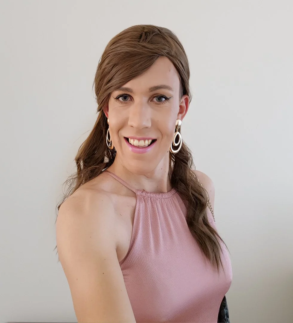 Lauren van Essen, long brown hair, wearing large hoop earrings and a pink sleeveless top, smiling and looking at the camera against a plain background.
