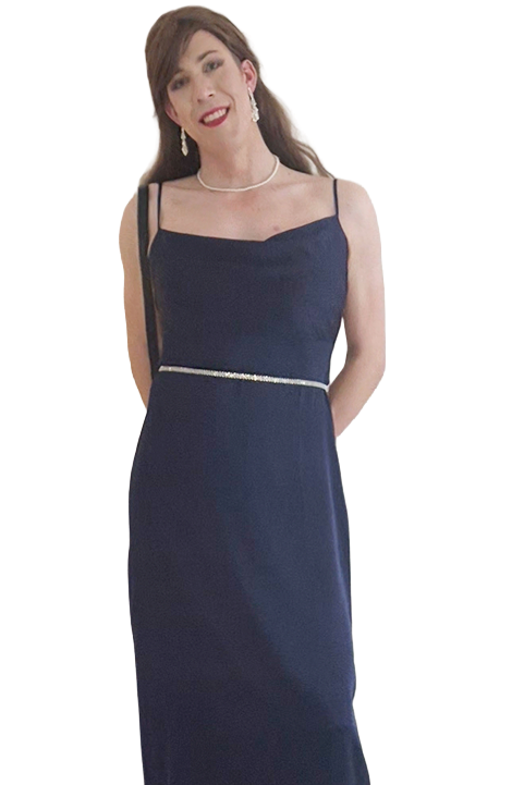 Woman in a navy blue evening gown with spaghetti straps, jewelry, and earrings, standing with hands behind her back.