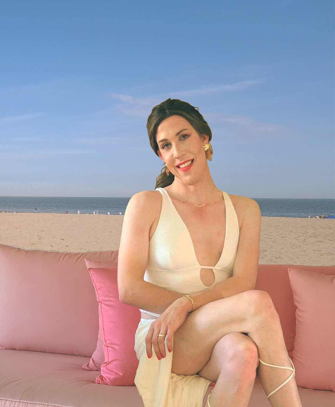 A woman sitting on a pink outdoor sofa near the beach during daytime, with the ocean and sky in the background.