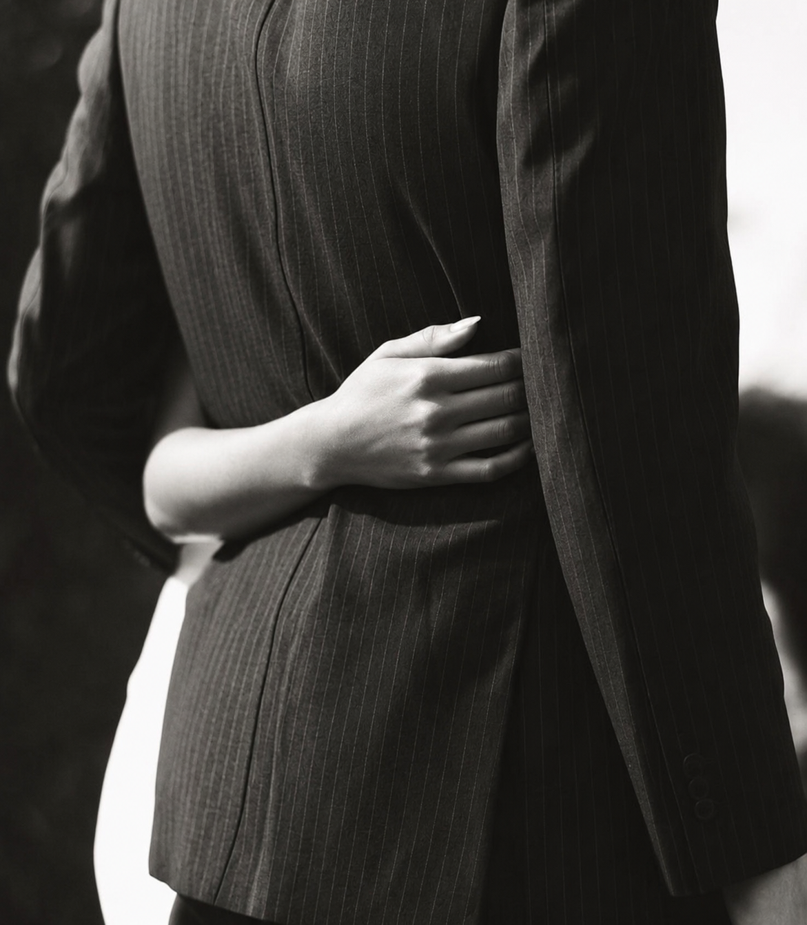 Close-up of a person's hand resting on their side, dressed in a pinstripe suit, in black and white.