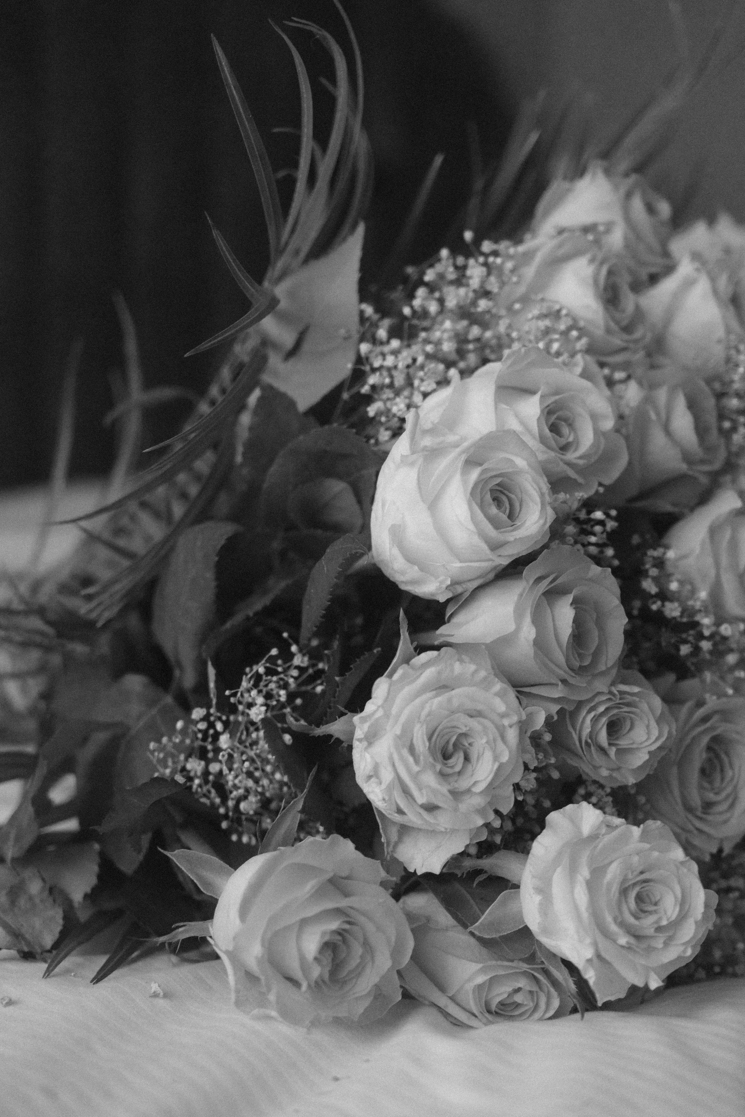 Blumengesteck mit weißen Rosen, kleinen weißen Blumen und grünen Blättern, auf einem weißen Tisch.