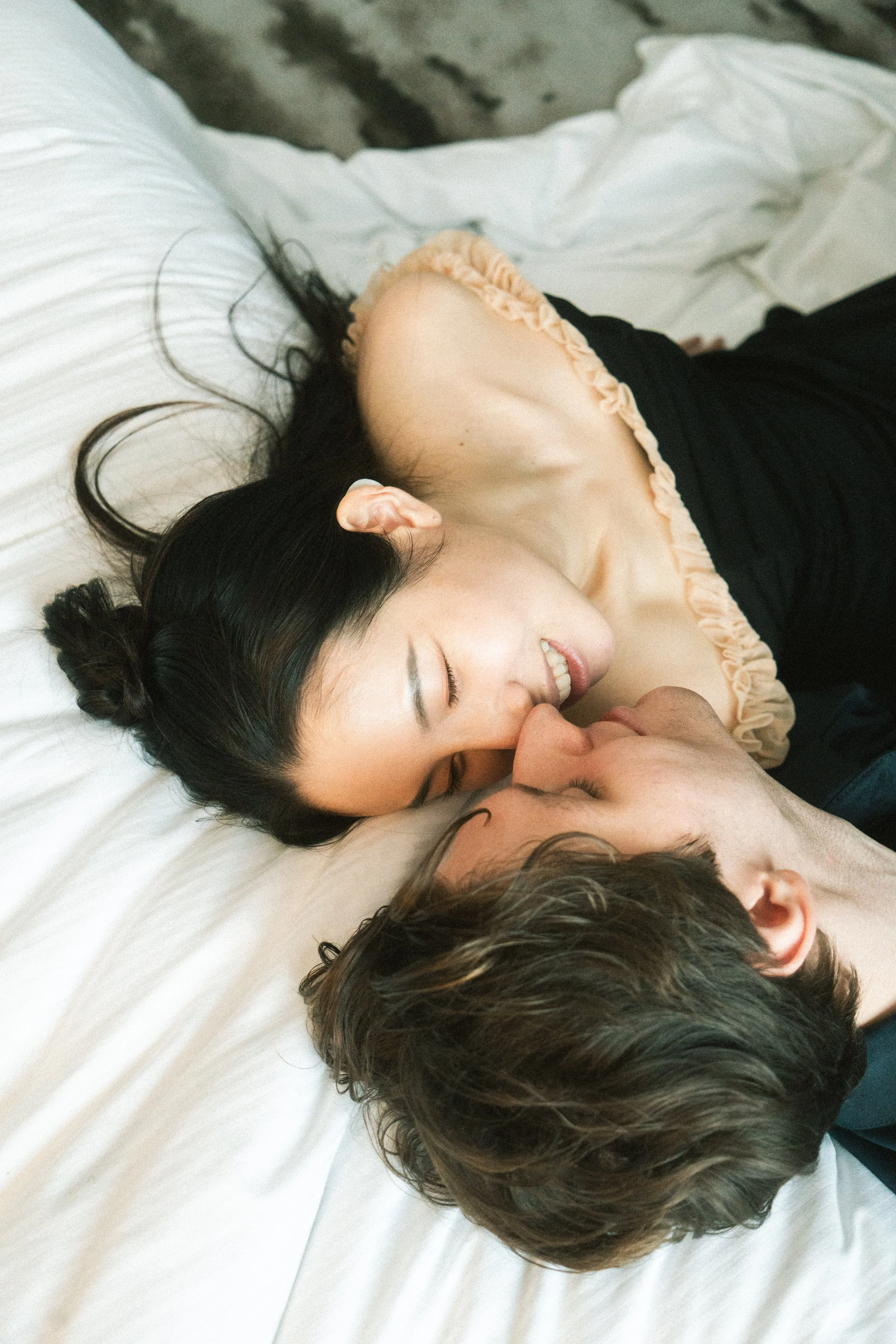 Zwei Frauen und ein Mann küssen sich auf einem Bett, alle mit geschlossenen Augen und glücklichen Ausdrücken.