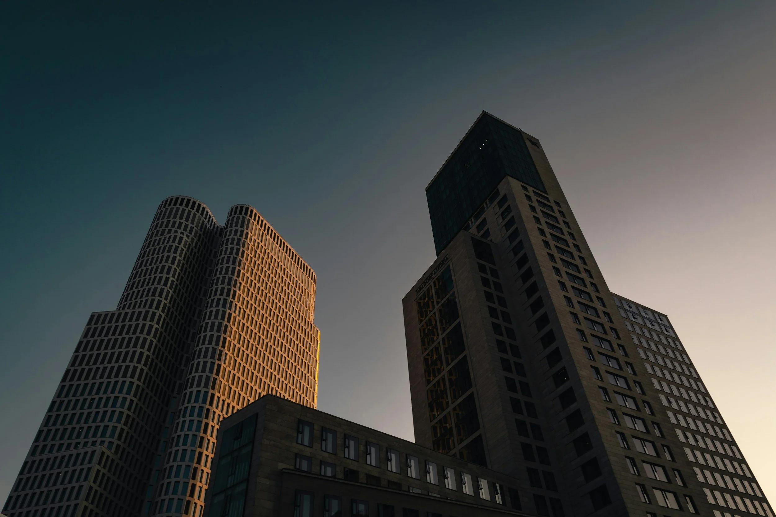 Une photo de bâtiments modernes vue en contre-plongée au crépuscule, avec un ciel clair et dégradé du bleu au gris.