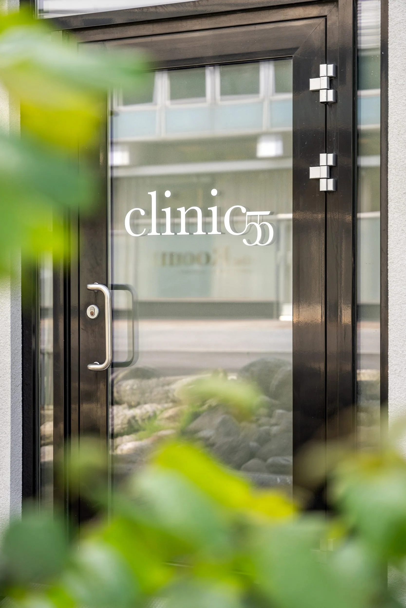 Nærbilde av en glassdør til en klinikk med teksten 'clinic 55' på glasset, omgitt av mørkt rammeverk.