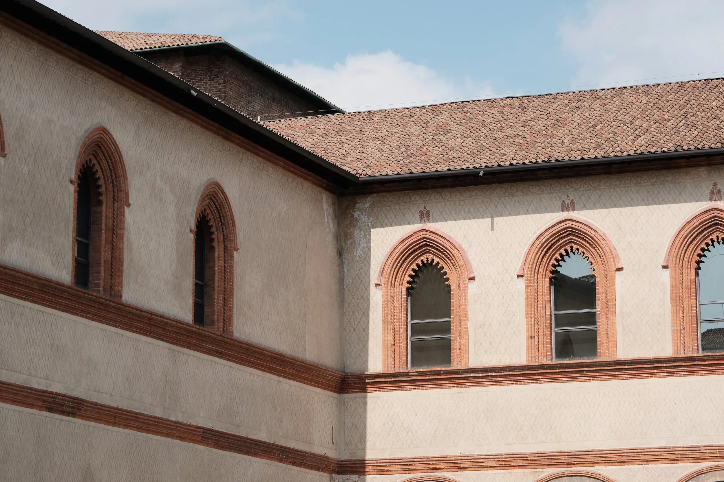 Close-up view of a building with arched windows and intricate brickwork details, featuring a light-colored facade with decorative patterns and a red-tiled roof.
