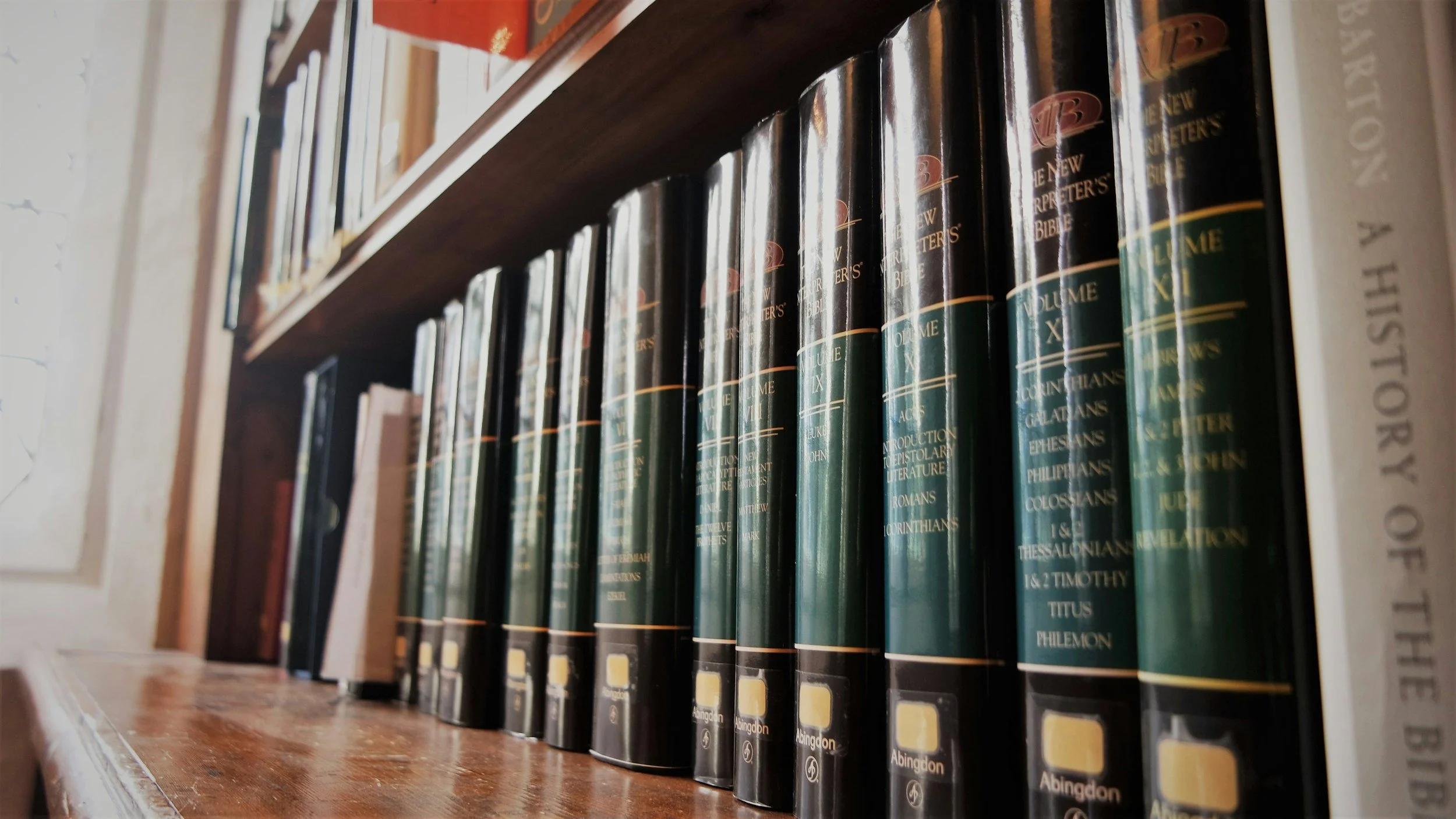 Bücherregal mit schwarzen Büchern, die den Titel 'The New Interpreter's Bible' tragen, auf einem Holztisch in einer Bücherei oder Buchhandlung.