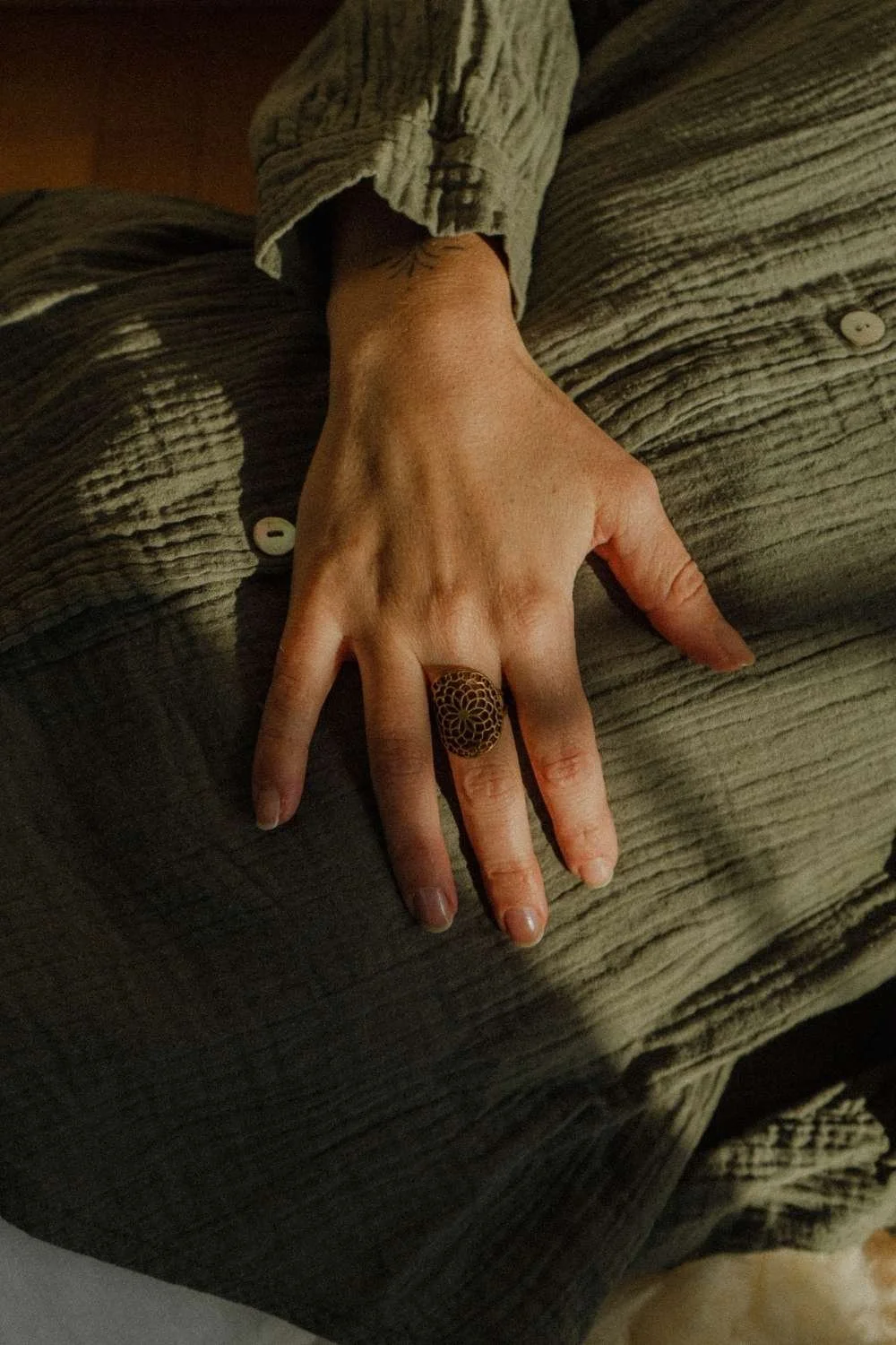Nahaufnahme einer Hand mit einem großen, schwarzen Ring mit Blume des Lebens Mustern.