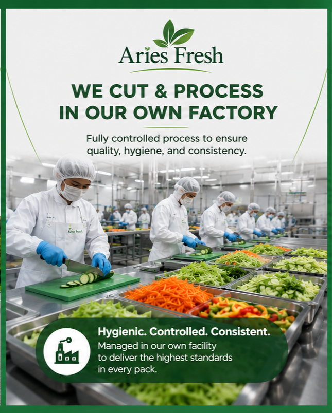 Workers in white uniforms, hair nets, and masks prepare sliced cucumbers, carrots, and greens in a clean, controlled factory setting.