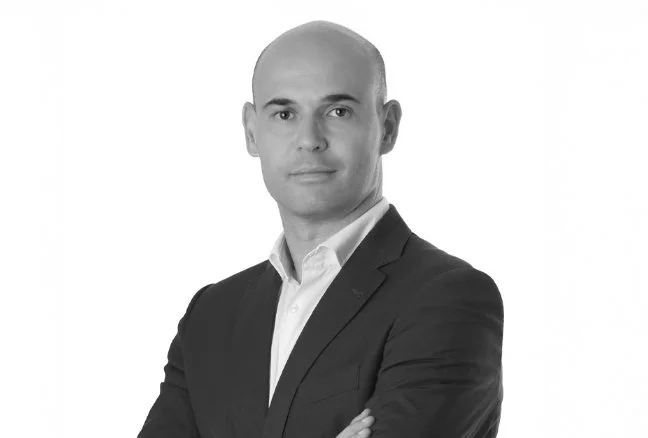 Black and white professional headshot of a bald man in a suit with arms crossed, looking at the camera.