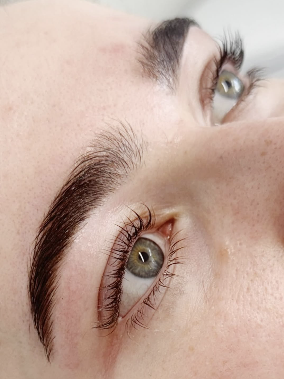 Close-up of a person's face showing well-groomed eyebrows and green eyes with long eyelashes.