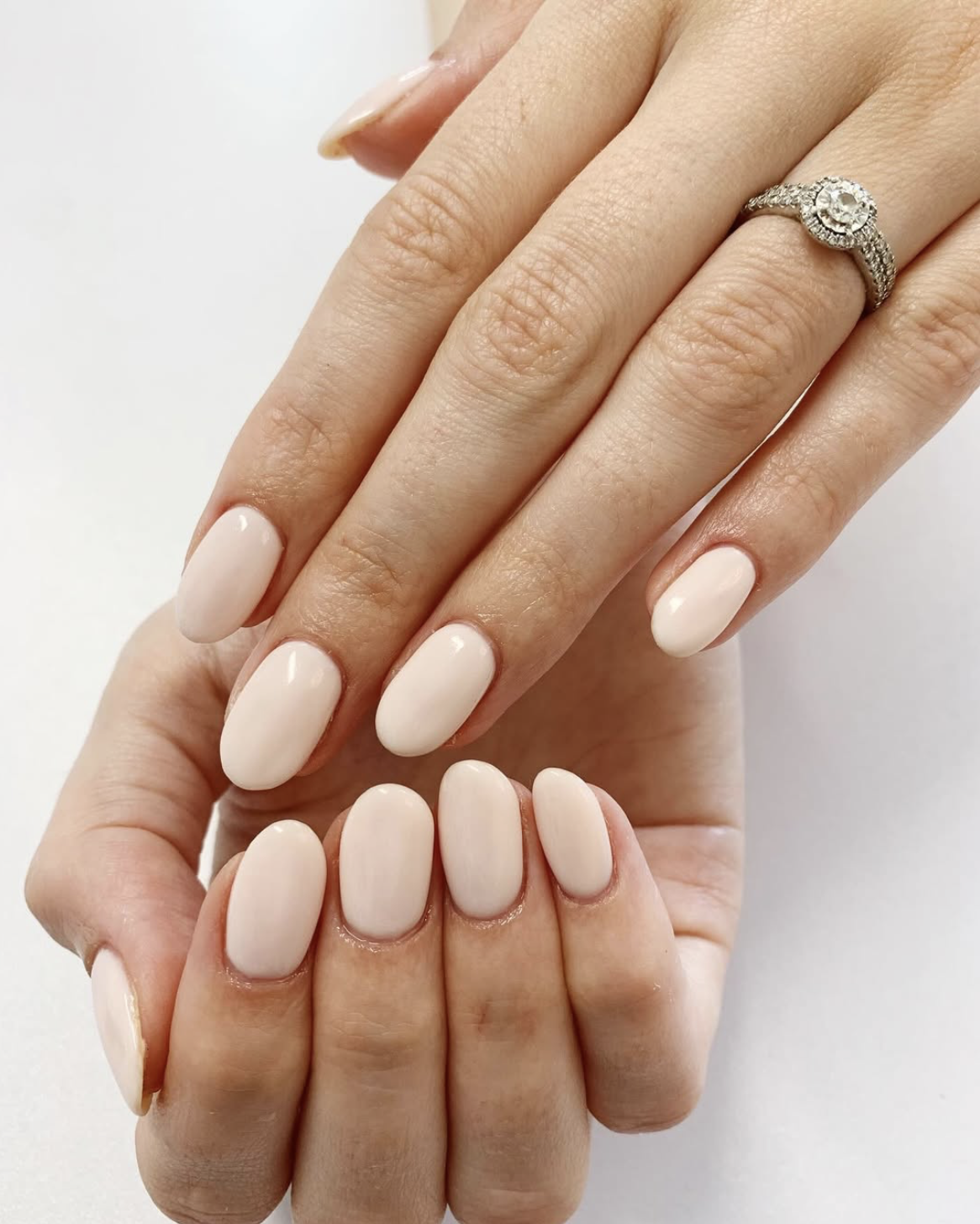 Close-up of a woman's hand with manicured nails, wearing a silver ring with a large central diamond surrounded by smaller diamonds.