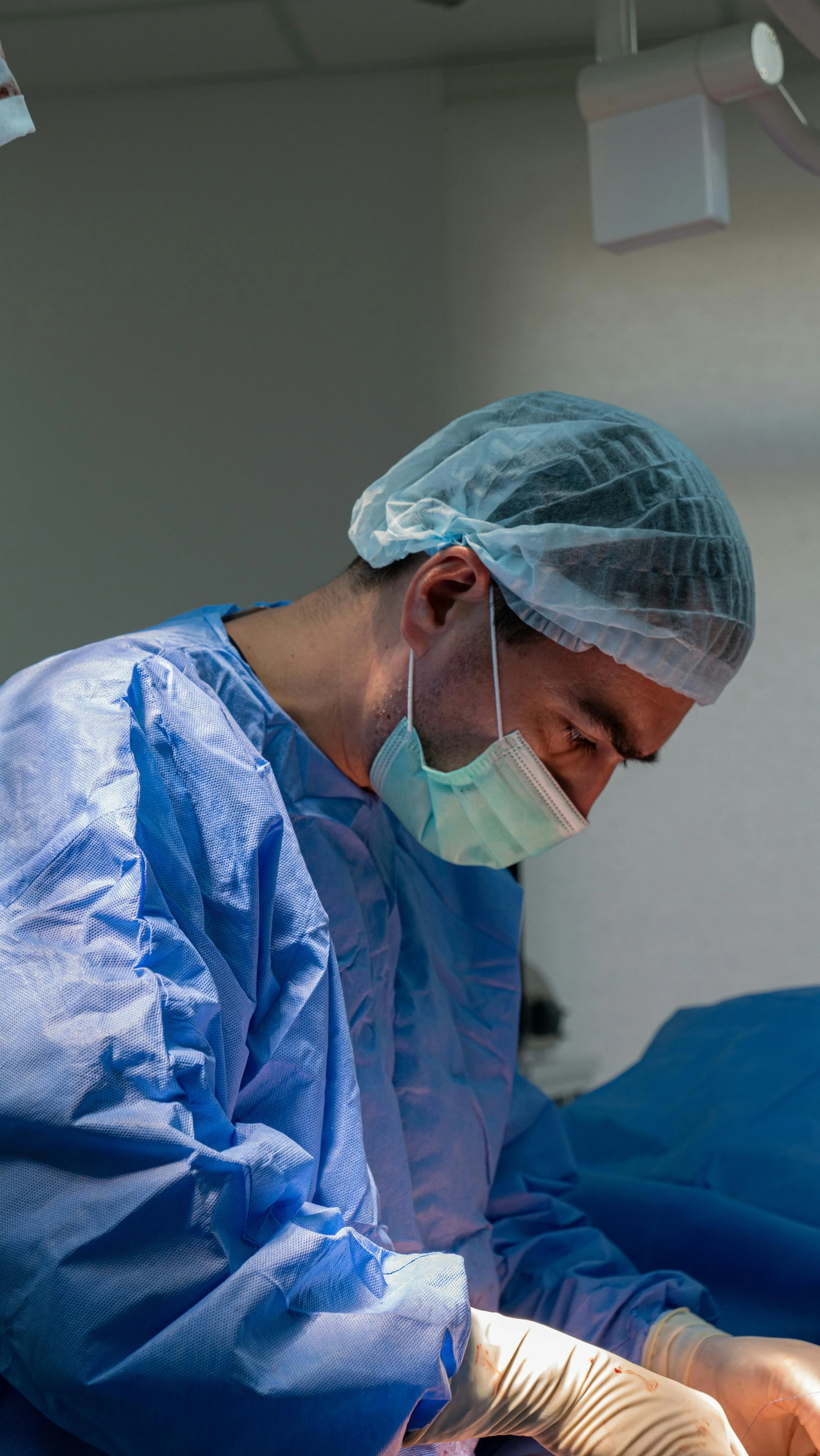 A surgeon wearing a surgical cap, face mask, and sterile gown performing a surgery in an operating room.