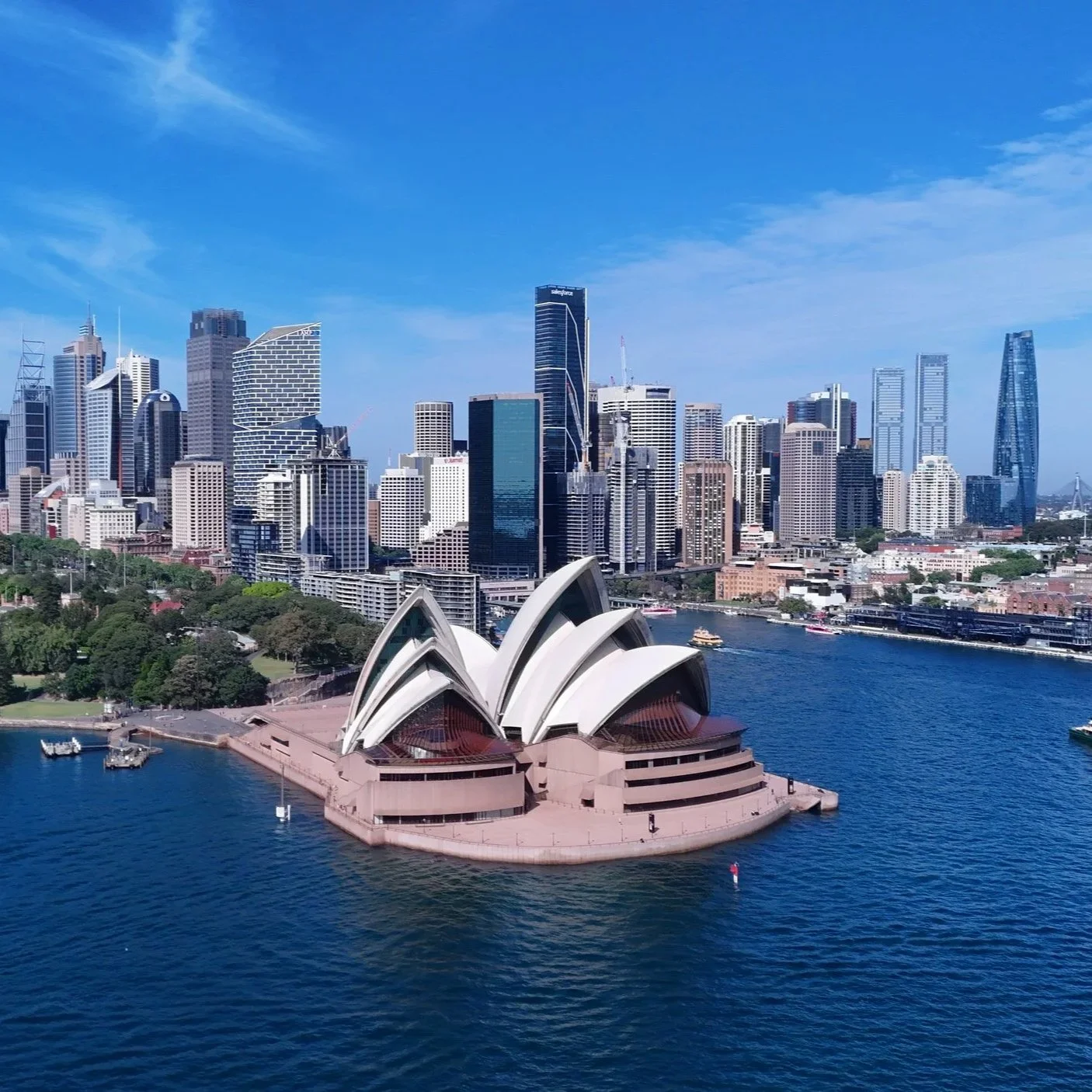 Vue aérienne de Sydney avec l'opéra de Sydney en premier plan et la skyline de la ville en arrière-plan sous un ciel bleu.