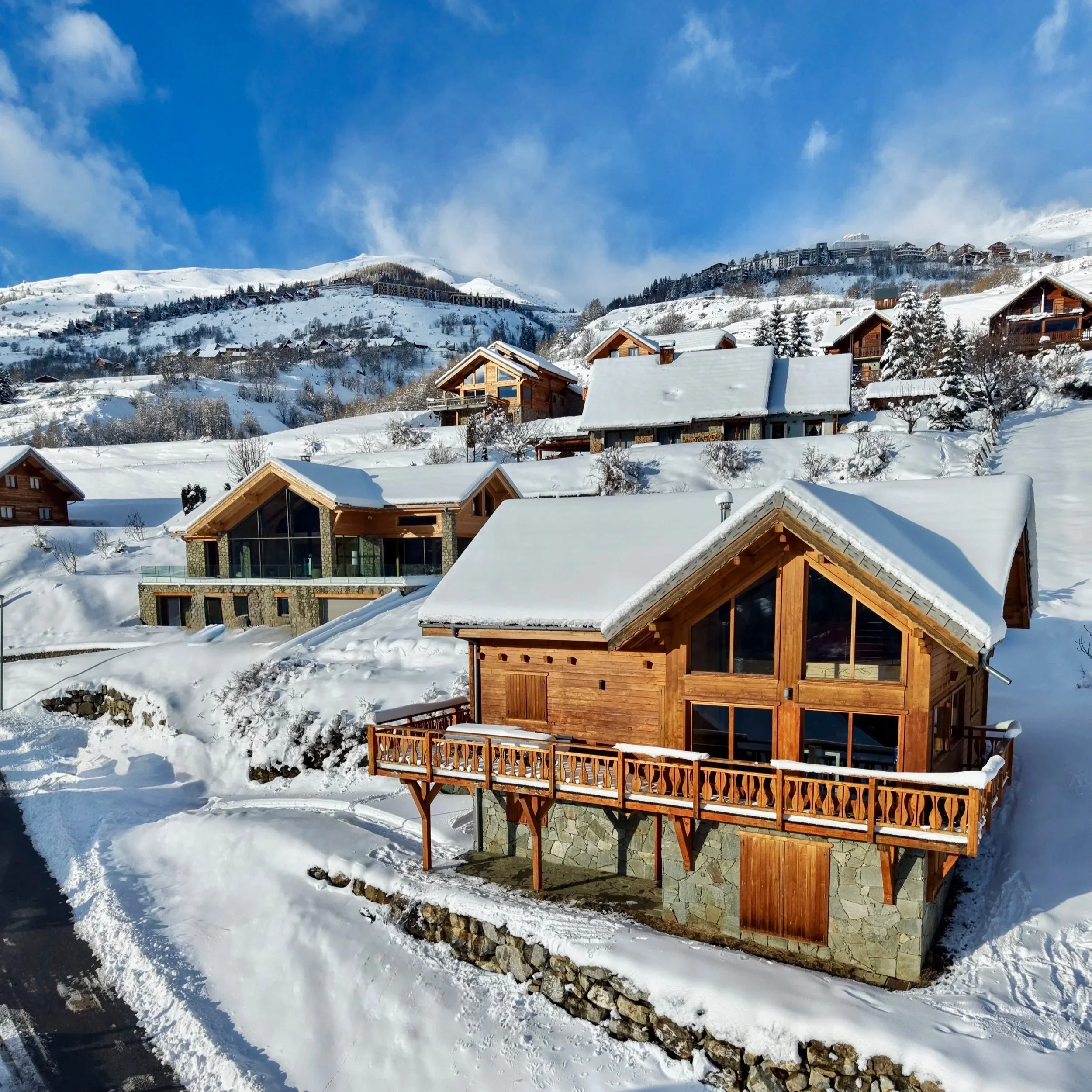 Chalet en bois avec toits enneigés, dans un paysage de montagne sous un ciel bleu avec quelques nuages.