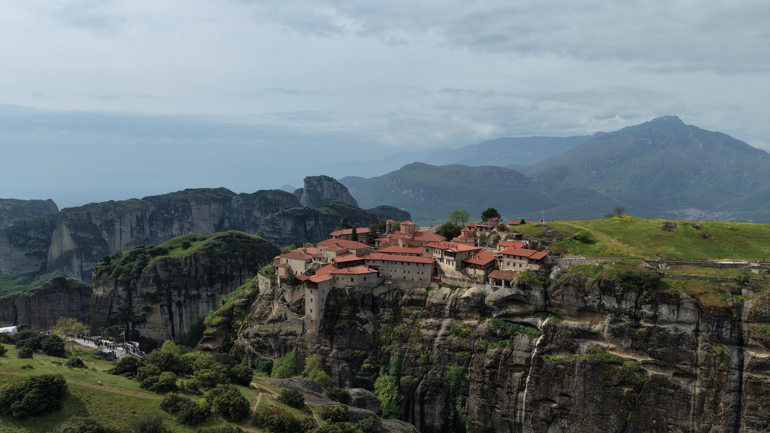 Village perchée en Grèce dans les Météores avec des maisons à toit rouge et un paysage verdoyant.