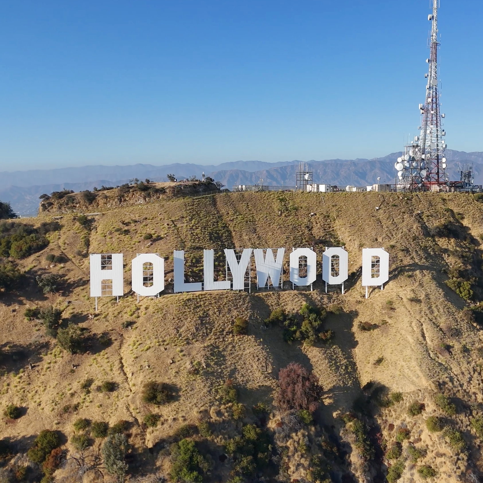 Le panneau Hollywood écrit en grandes lettres blanches sur une colline avec des antennes et des montagnes en arrière-plan
